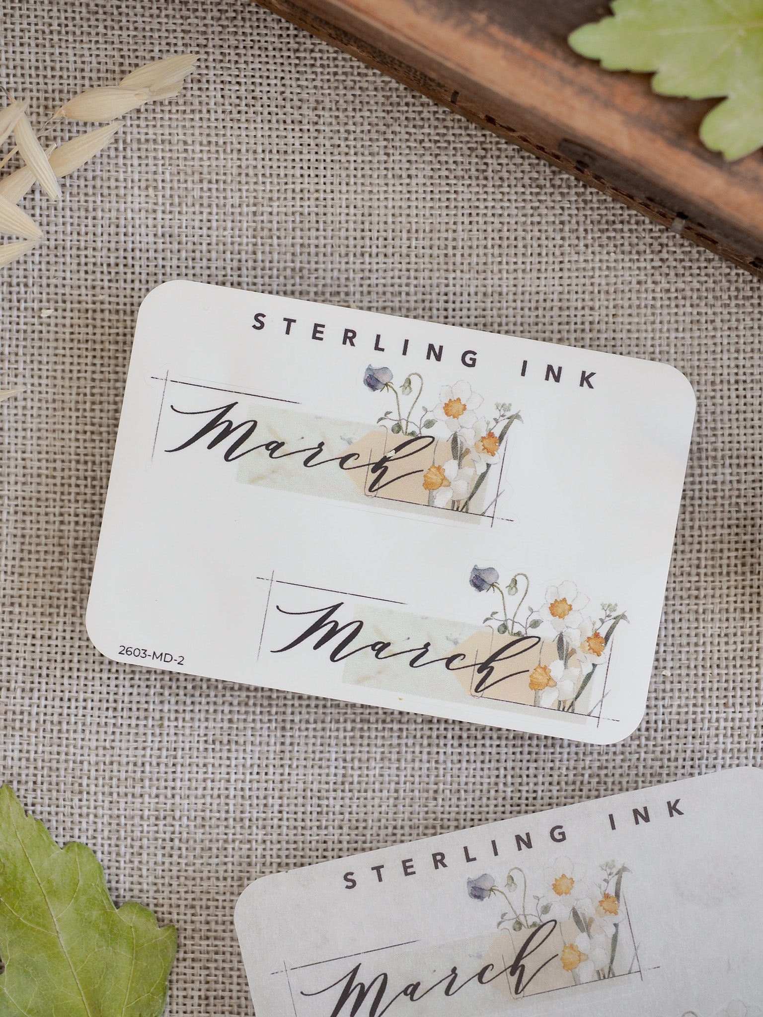 Decorative March sticker featuring "Sterling Ink" branding, elegant script, and soft watercolor illustrations of yellow and purple wildflowers.