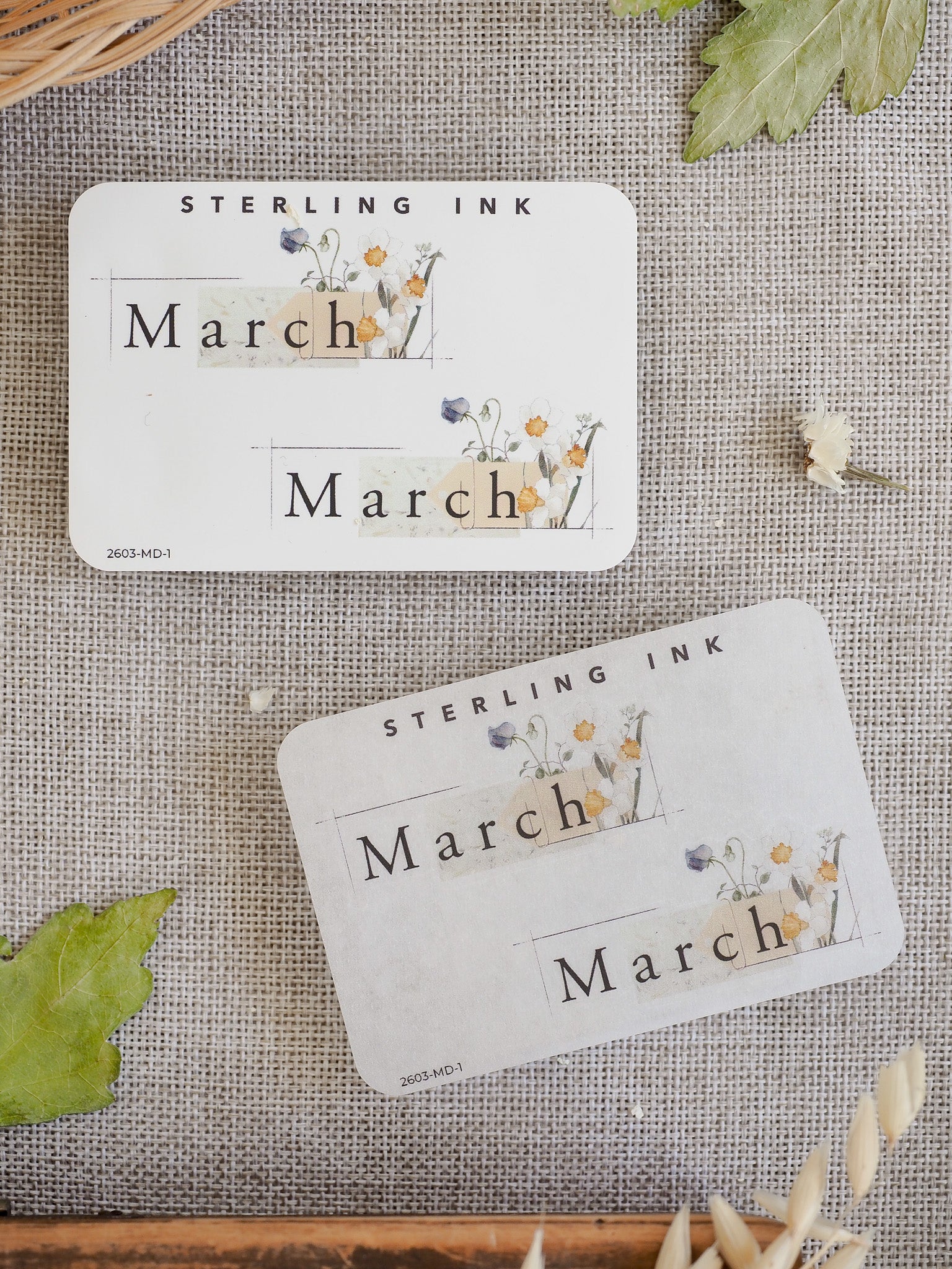 Spring-themed "March" sticker featuring delicate watercolor florals, greenery, and soft pastel accents on an off-white background.