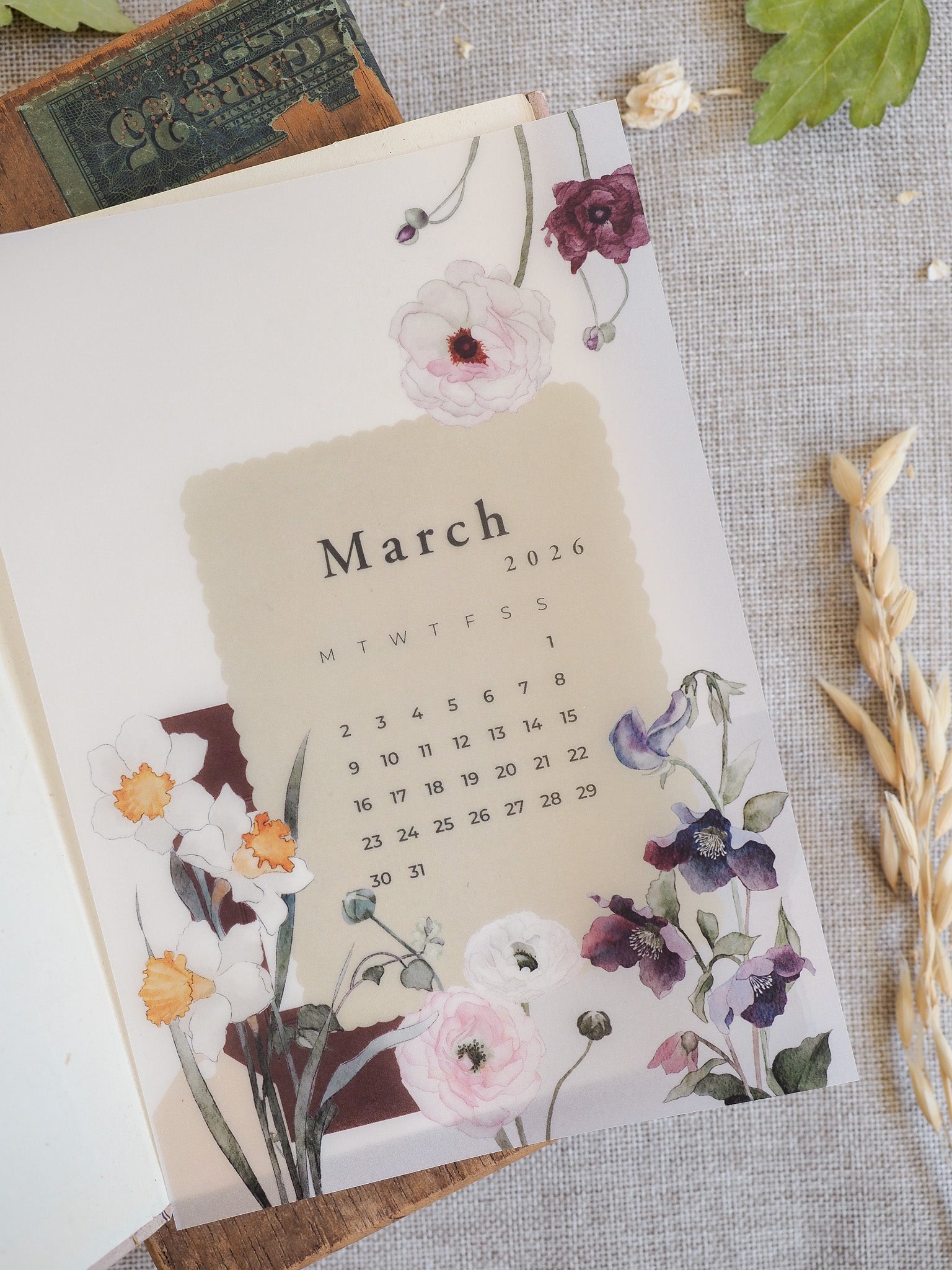 Watercolor calendar page for March 2026 featuring delicate blooms of pink, purple, and white flowers surrounding the month layout.