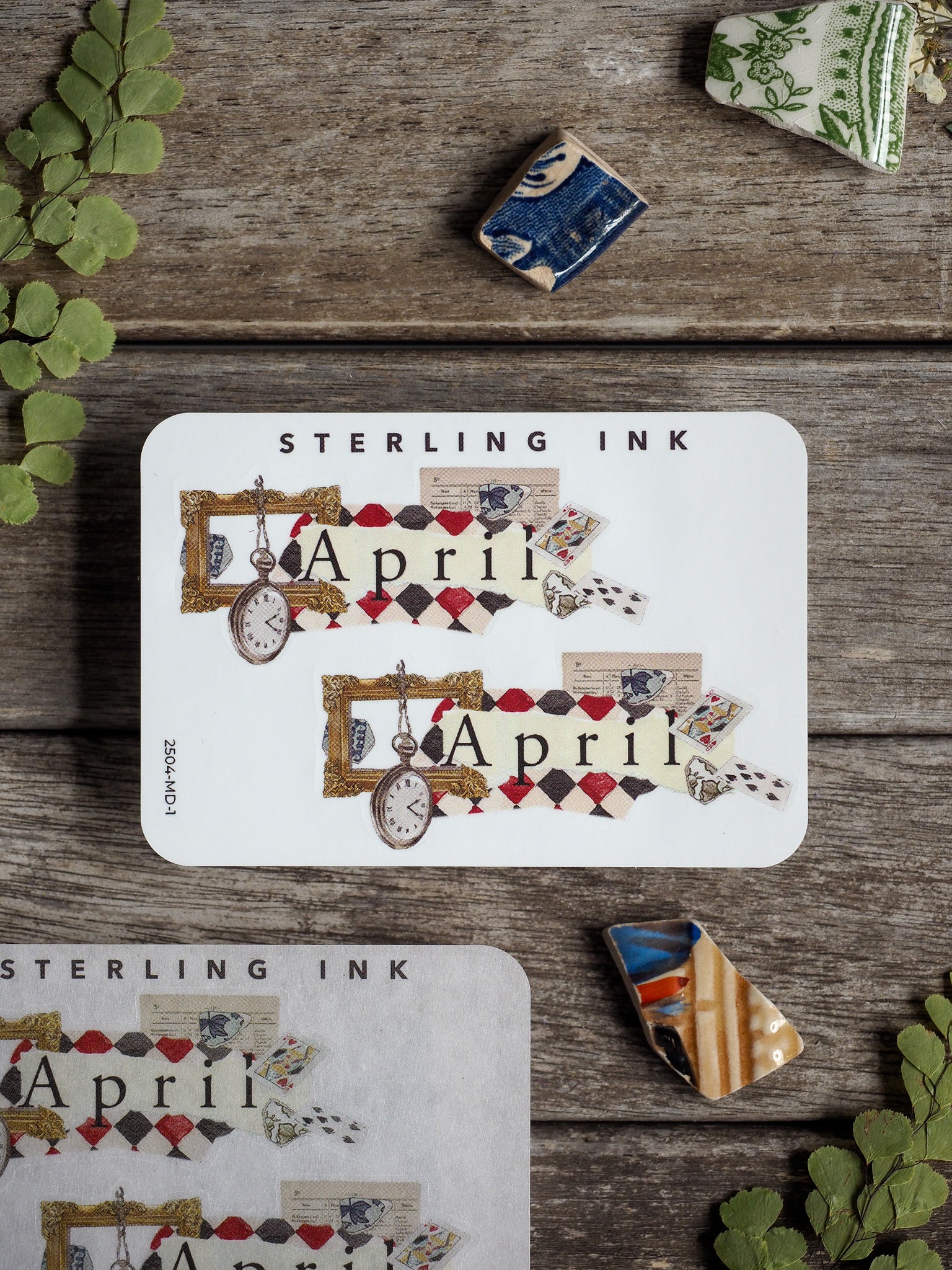 A decorative white sticker featuring a vintage "April" theme with patterned borders, assorted small ephemera, and a central analog clock motif, perfect for scrapbooking or journaling.