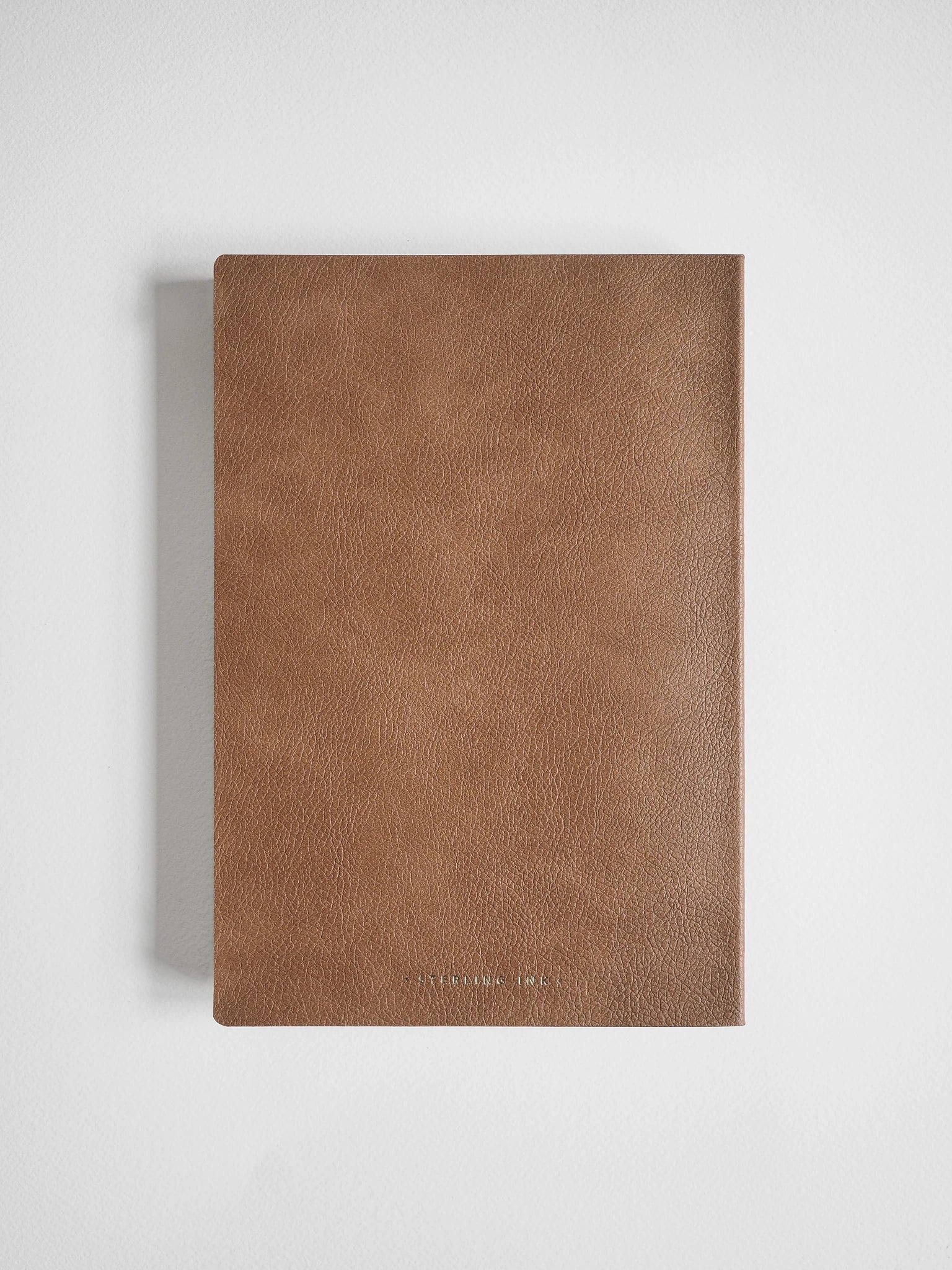 A brown textured leather notebook or journal with a minimalist design, shown closed on a light gray background.
#Color_Caramel