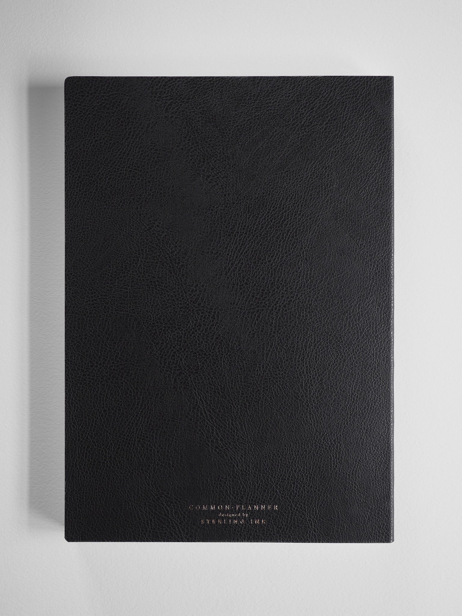 Sleek black academic planner with a textured faux-leather cover, featuring minimalist gold foil lettering that reads "Common Planner" and is designed for the 2026-2027 year.
