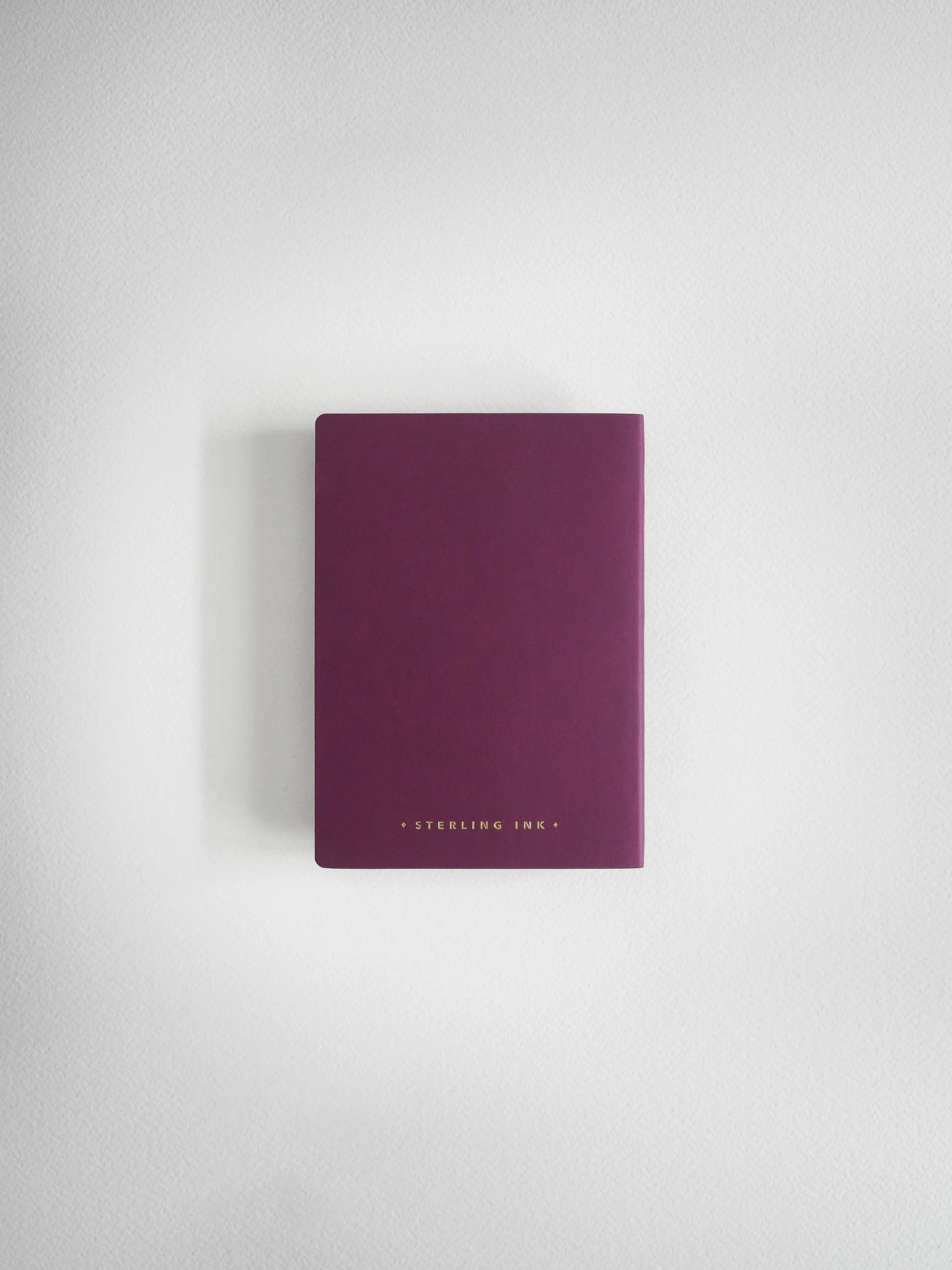 A slim, matte dark purple notebook or journal with gold foil text reading 'STERLING HINE' at the bottom, centered against a light gray textured background.
#Color_Mulberry