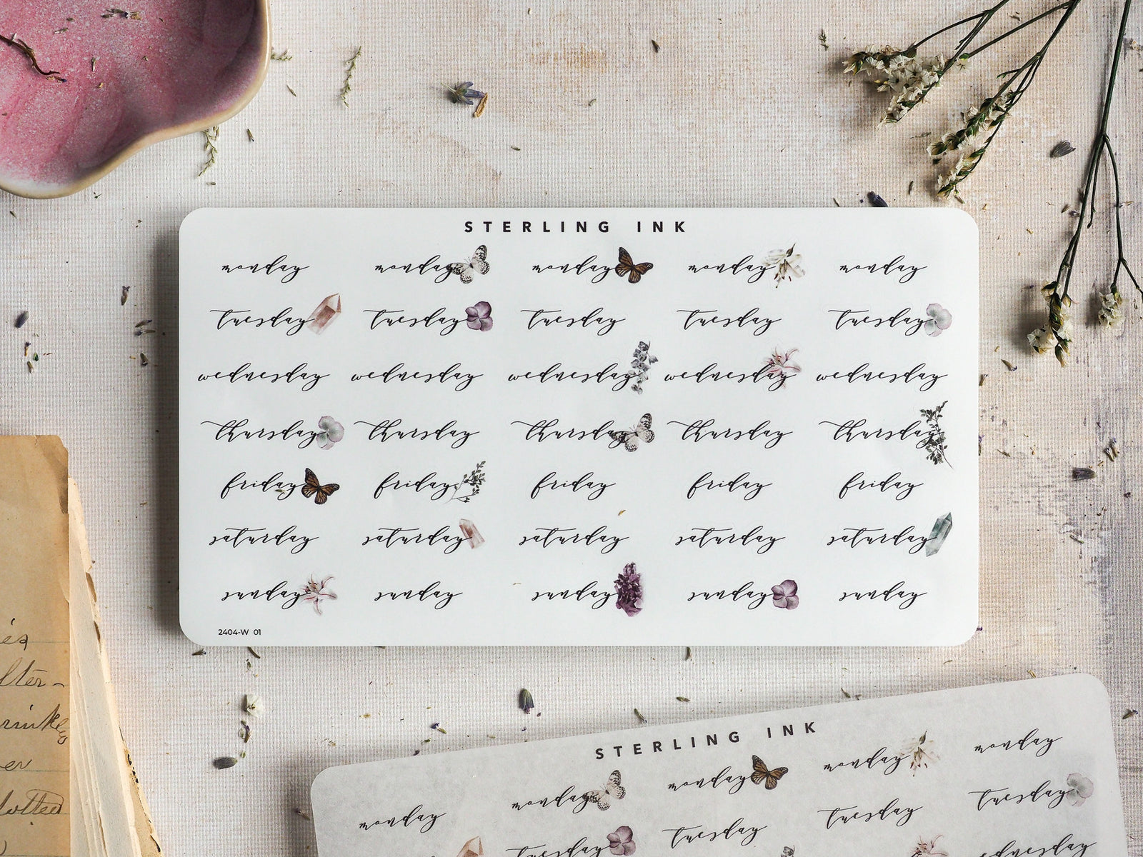 A set of aesthetic, white week day stickers featuring rustic typography and delicate, printed accents of florals and butterflies for journaling.