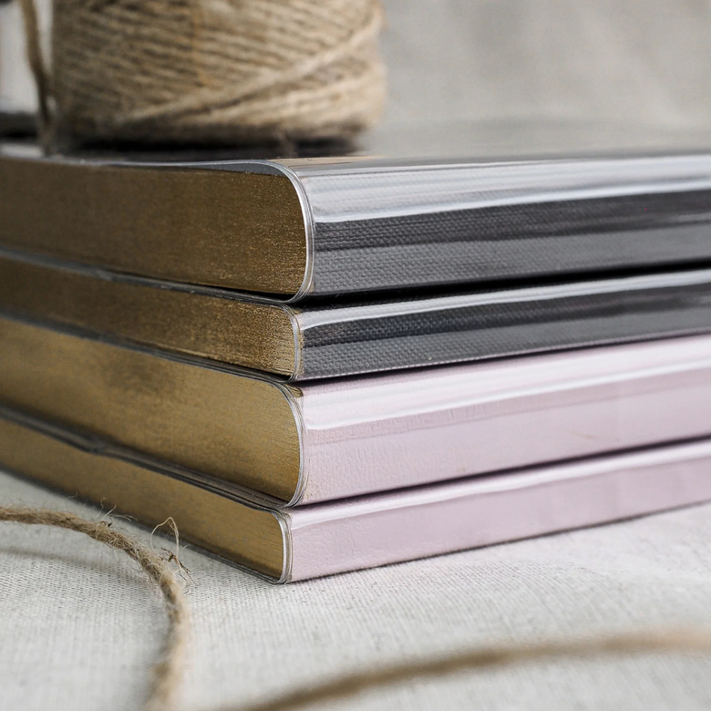 A stack of protective clear book covers showcasing varied neutral tones, including matte gold, sleek silver, and soft pastel pink.