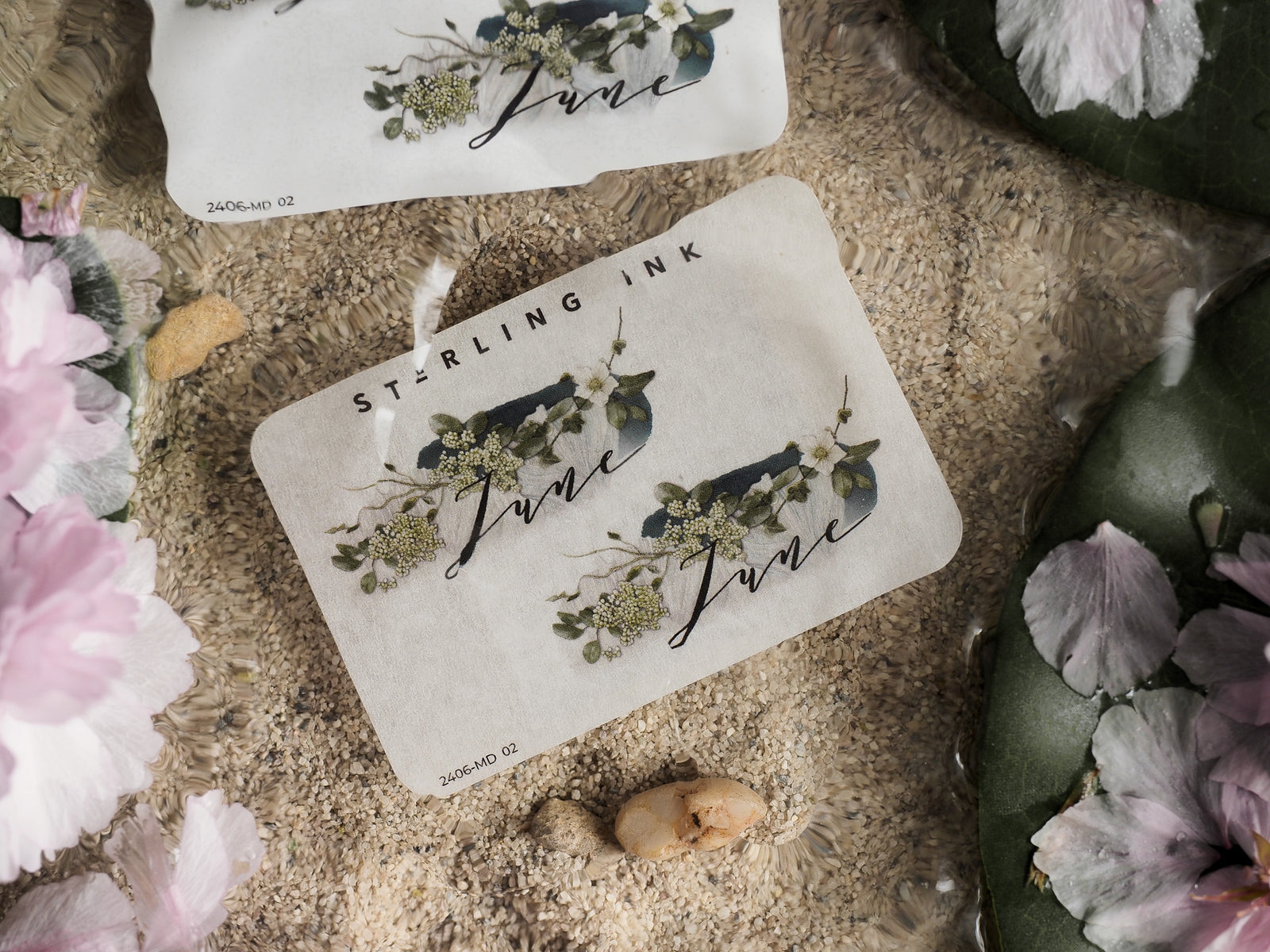 Elegant "June" month sticker featuring delicate watercolor greenery and small white flowers, perfect for scrapbooking or journaling.