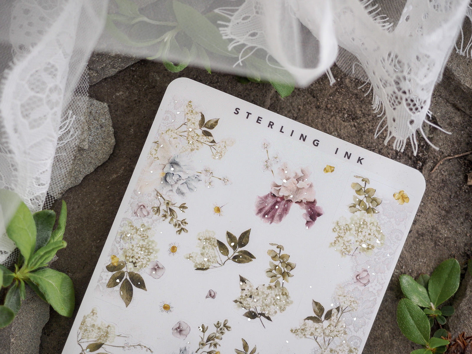 Detailed botanical washi stickers on white paper, featuring clustered designs of soft pink, ivory, and sage green blossoms and leaves with delicate gold foil accents.