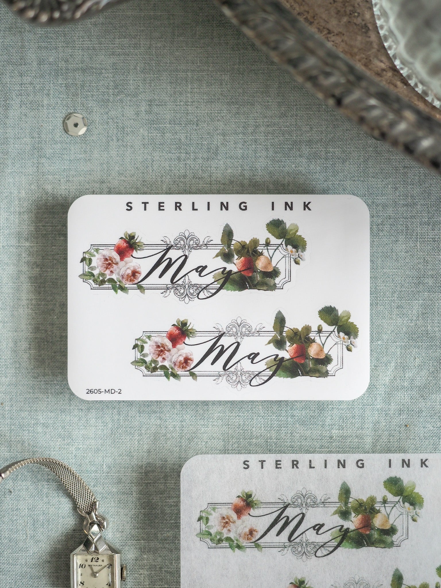 White floral sticker featuring the word "June" in elegant script, framed by watercolor blooms of pink and red flowers, lush greenery, and small berries for a spring theme.