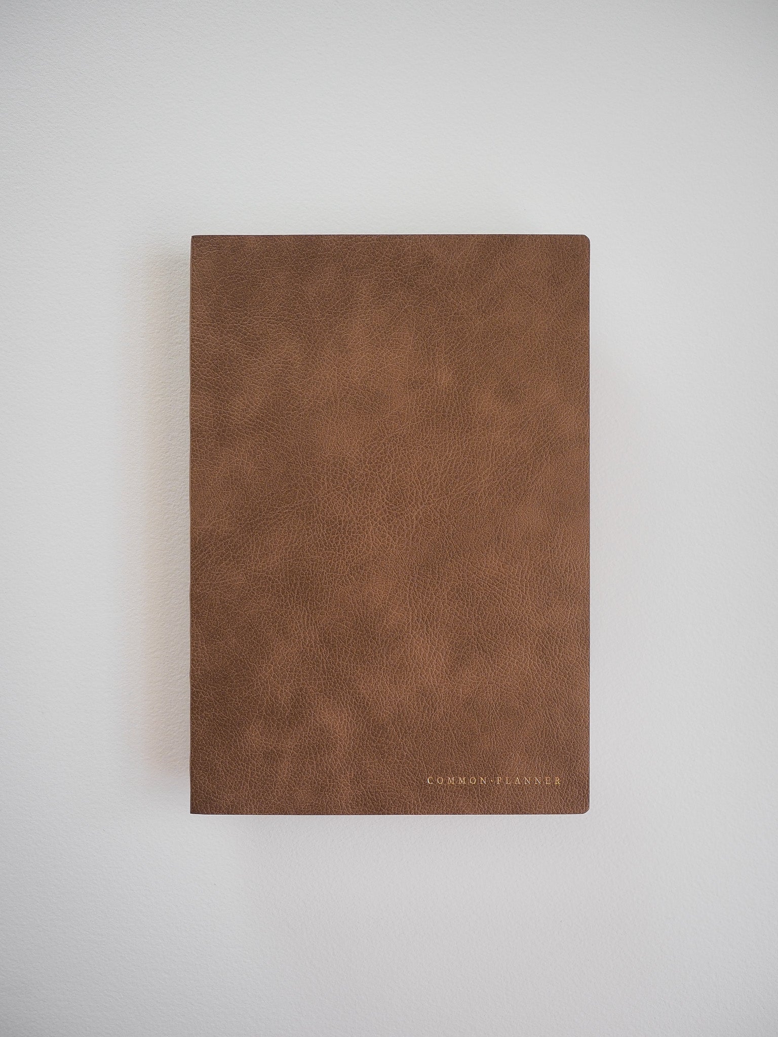 Elegant A5 vertical planner with a warm, cognac faux-leather cover, featuring minimalist branding centered near the bottom edge.