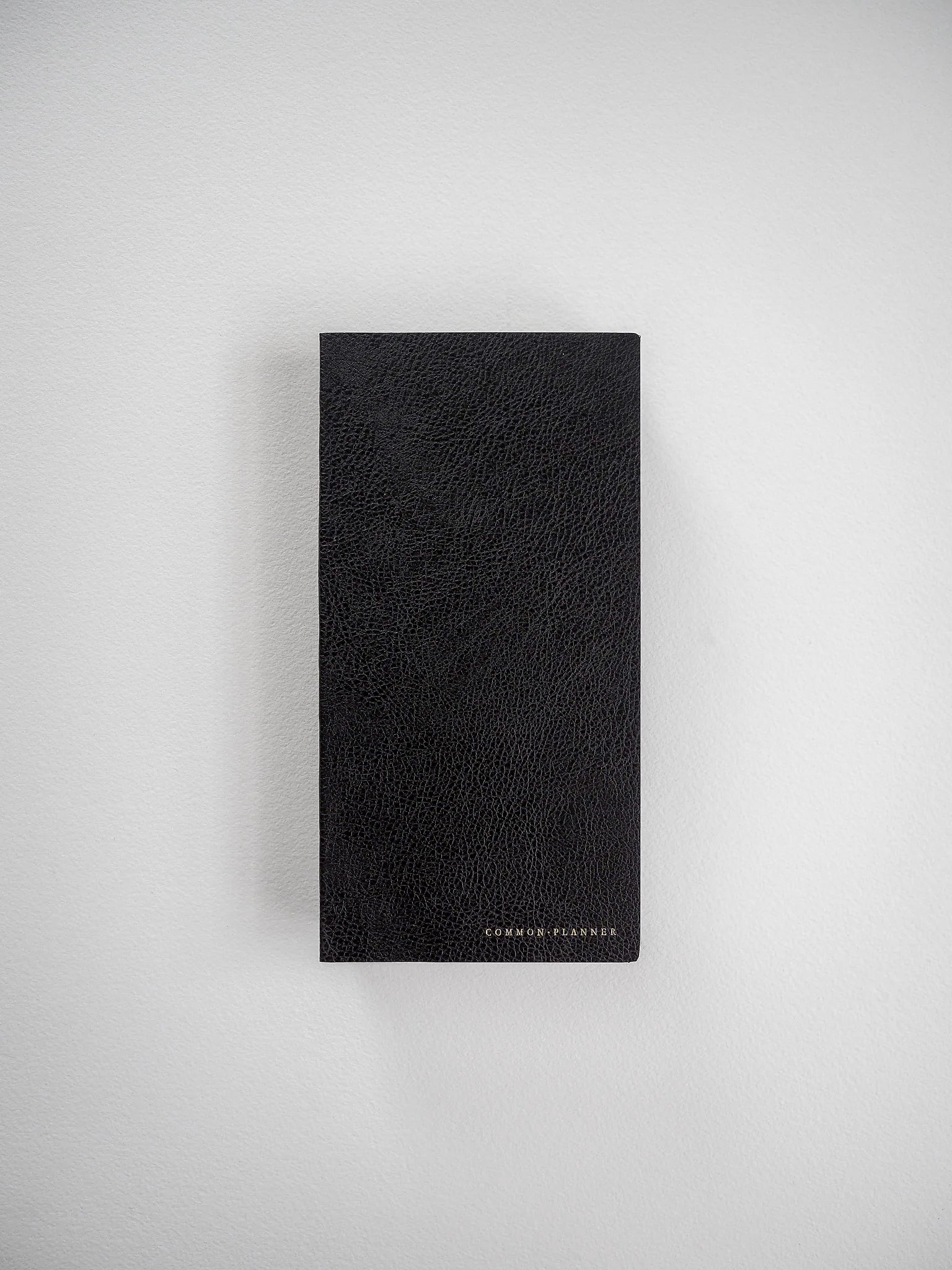 Elegant black planner notebook with a pebbled, faux-leather texture, featuring a solid, minimalist design and subtle branding at the base.