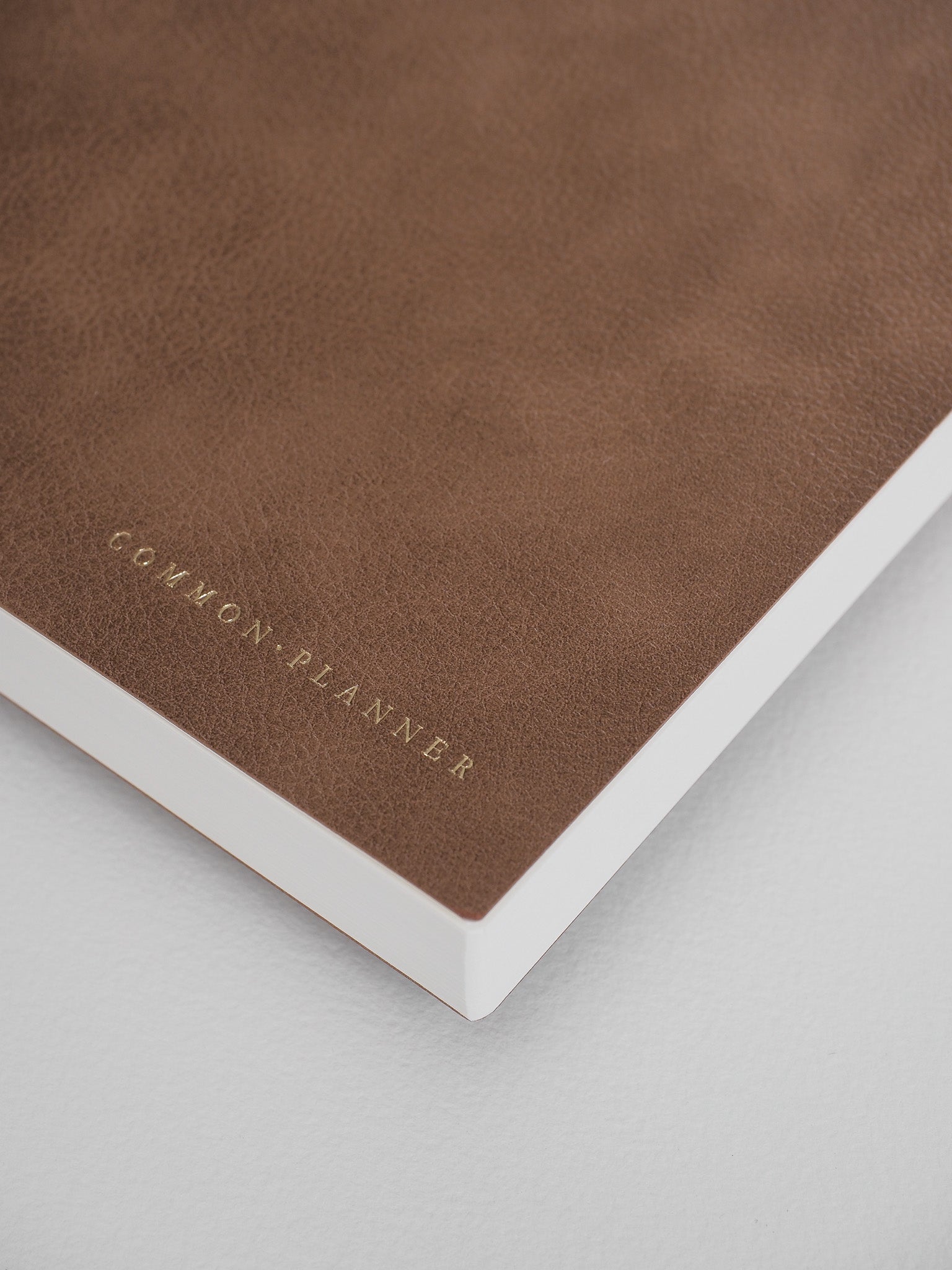 Minimalist, cocoa-brown planner with a textured cover, featuring the elegant, debossed text "COMMON PLANNER" centered on the front.