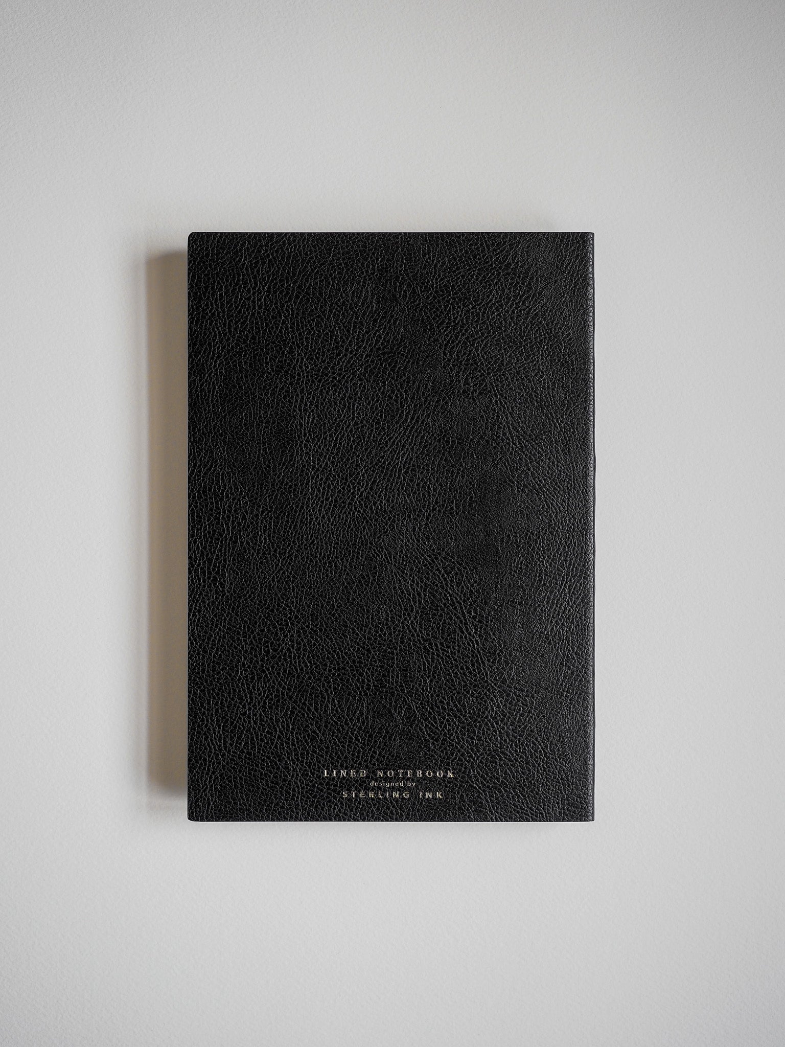 Deep black, textured A5 notebook featuring subtle, debossed gold lettering, perfect for writing and journaling.