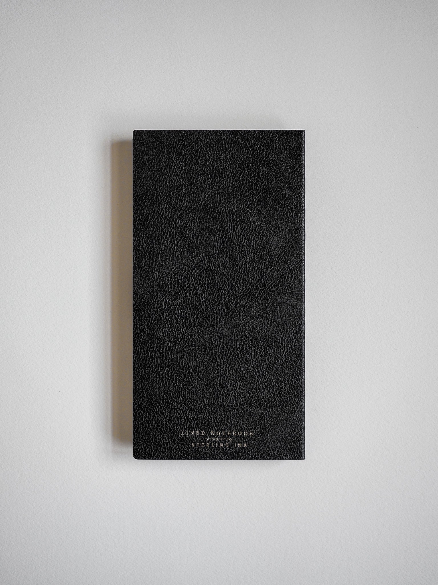 Sleek, black faux-leather notebook with a textured finish and elegant gold embossing, designed for writing and note-taking.