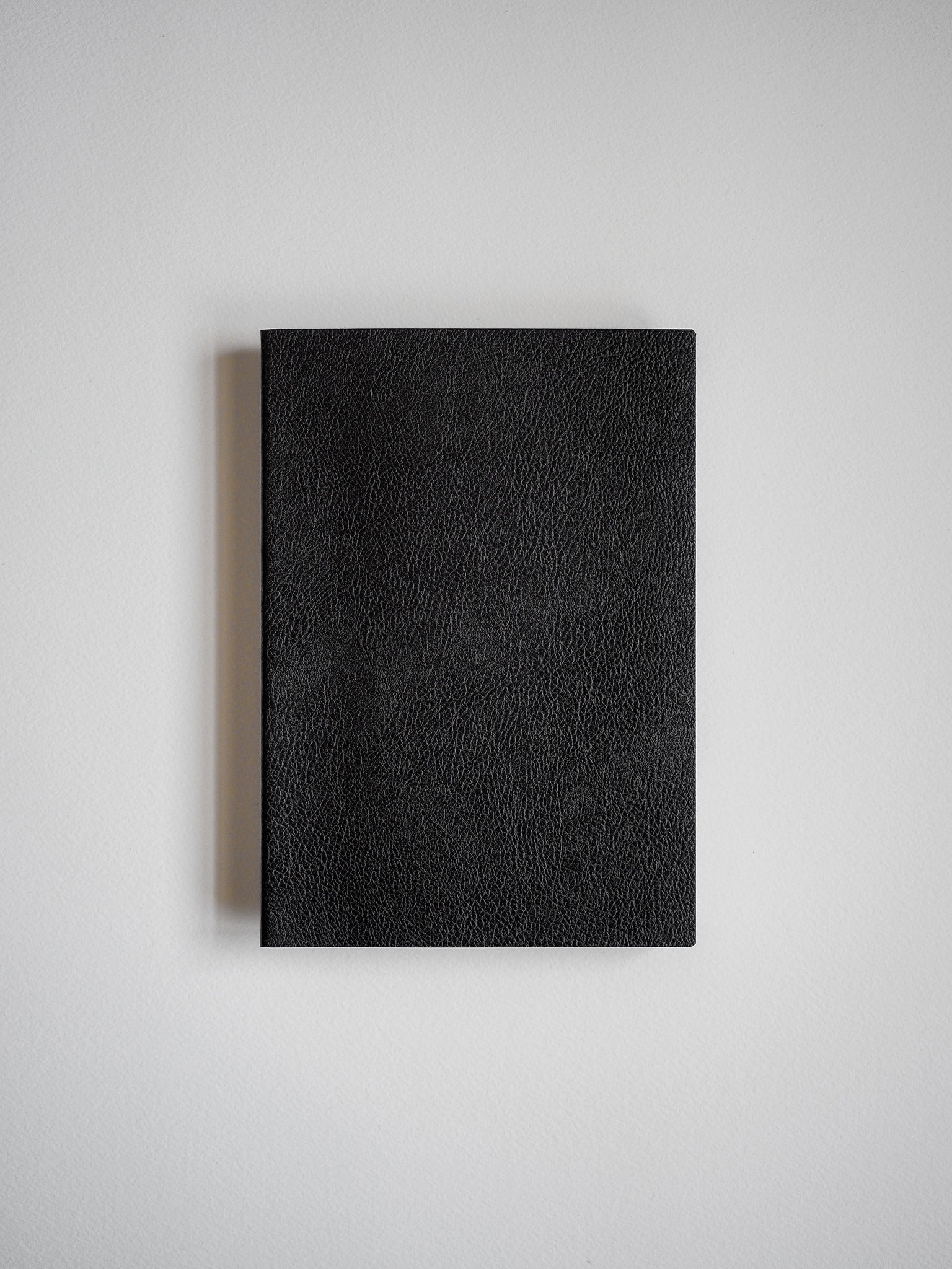 Solid black notebook featuring a textured, minimalist faux leather cover, designed for writing, journaling, or work notes.