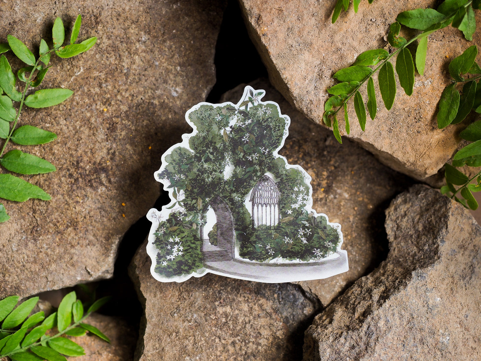 Detailed die-cut vinyl sticker featuring a whimsical garden gate framed by lush green foliage, perfect for cottagecore or nature themes.