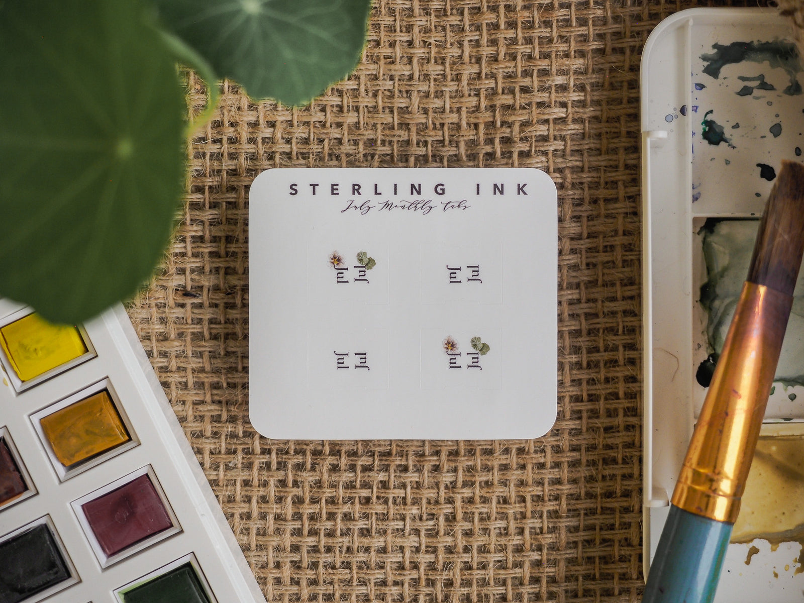 Delicate planner sticker set featuring "July Monthly Tabs" on a white card, decorated with small, subtle black floral and leaf motifs.