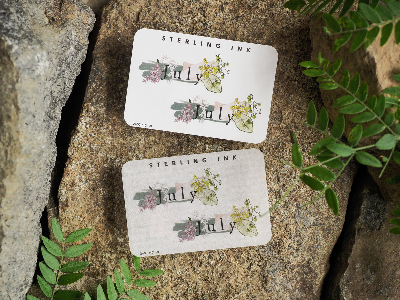 Decorative monthly sticker label for planners featuring the word 'July' surrounded by delicate watercolor blooms, soft pink accents, and lush green foliage.