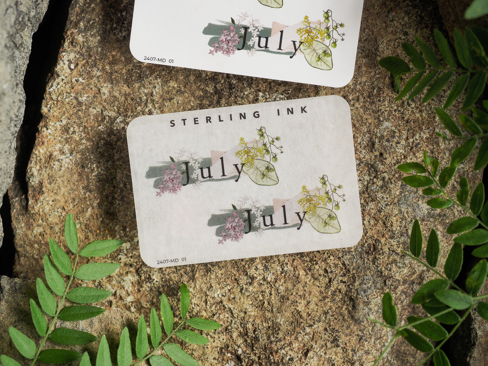 Botanical month sticker for July, featuring delicate watercolor accents of yellow and pink wildflowers printed on creamy, natural paper.