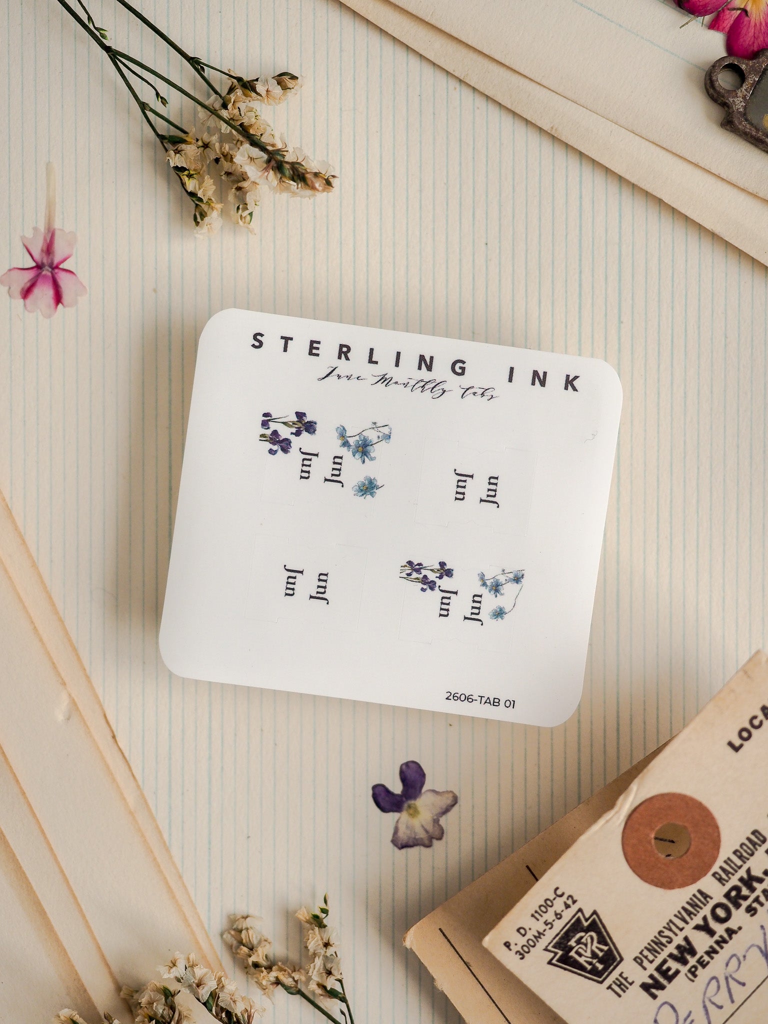 White sticker sheet from Sterling Ink featuring delicate, hand-drawn botanical illustrations of tiny blue and purple flowers, making a charming nature-themed stationery product.