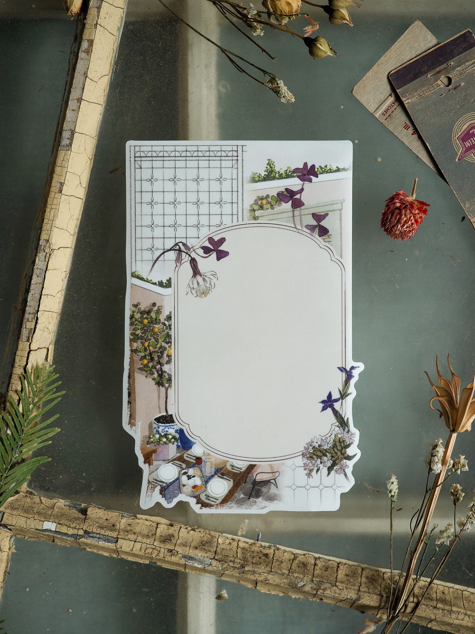 Seasonal decorative sticker featuring a cream-bordered frame, combining a subtle planning grid with a detailed floral vignette of purple blooms and rustic tabletop elements.