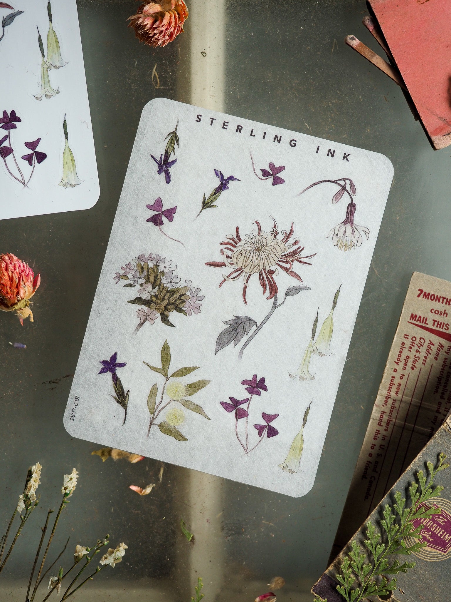 Botanical sticker sheet featuring various watercolor florals, including lilies, clustered purple blossoms, and a prominent central bloom, titled "Sterling Ink."