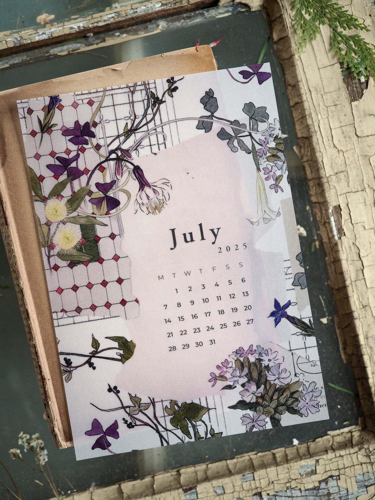Elegant B6 monthly calendar featuring a watercolor botanical wreath of purple and green florals surrounding the text "July 2025."