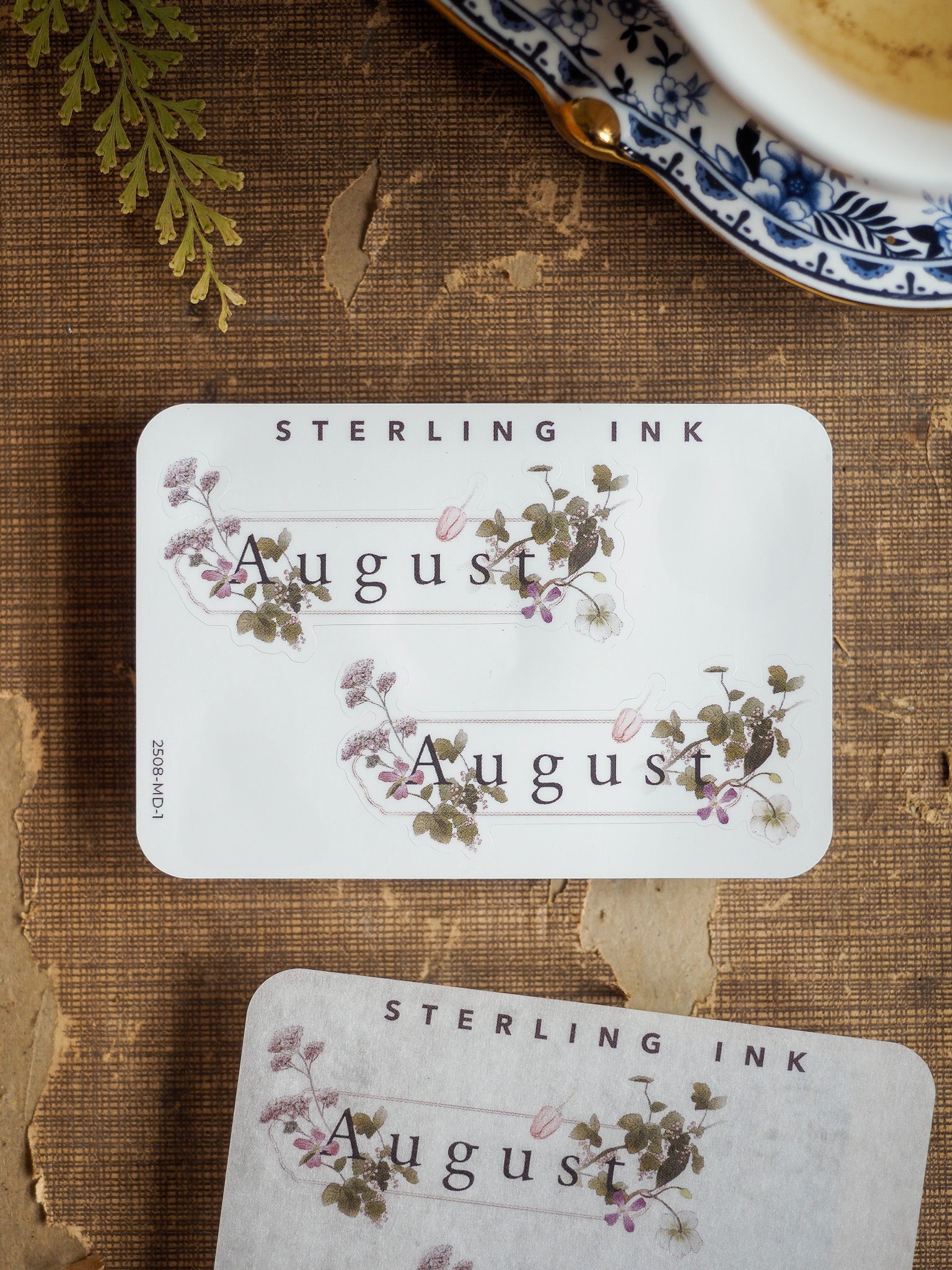 Aesthetic August planner sticker set featuring "Sterling Ink" text and delicate watercolor floral designs of purple and green leaves.