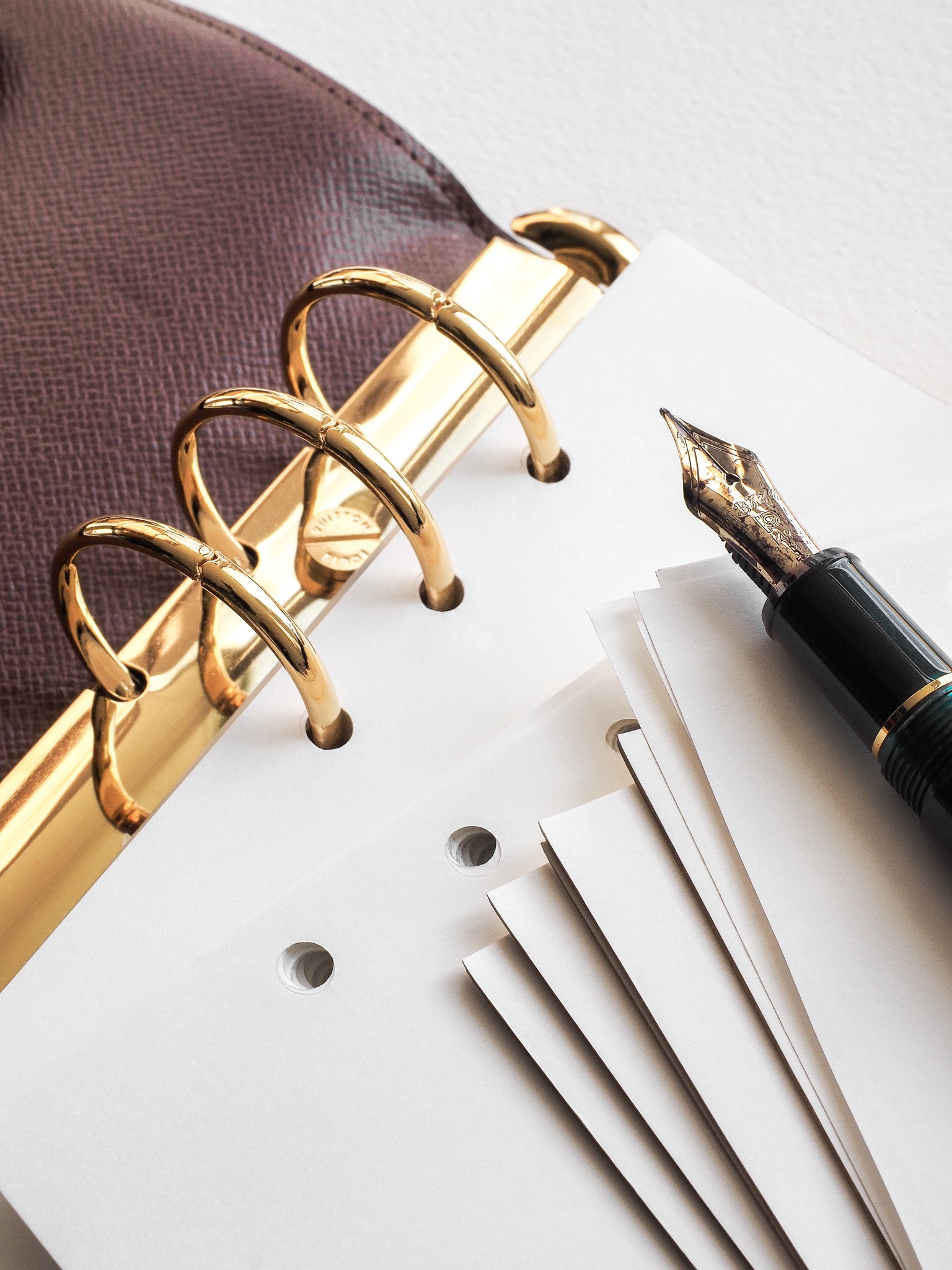 A stack of pristine, blank white loose leaf Tomoe River paper inserts secured by a gleaming gold ring binding mechanism.