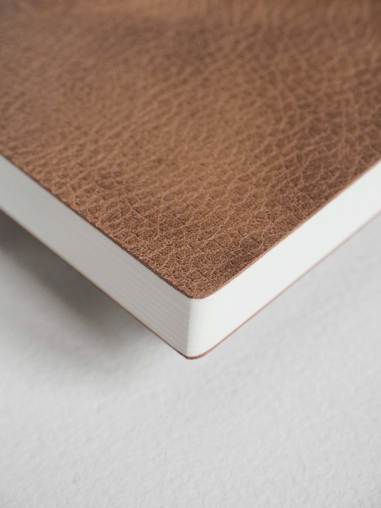 A closed A6 grid notebook featuring a textured, solid tan brown cover contrasted by crisp, visible white interior pages.