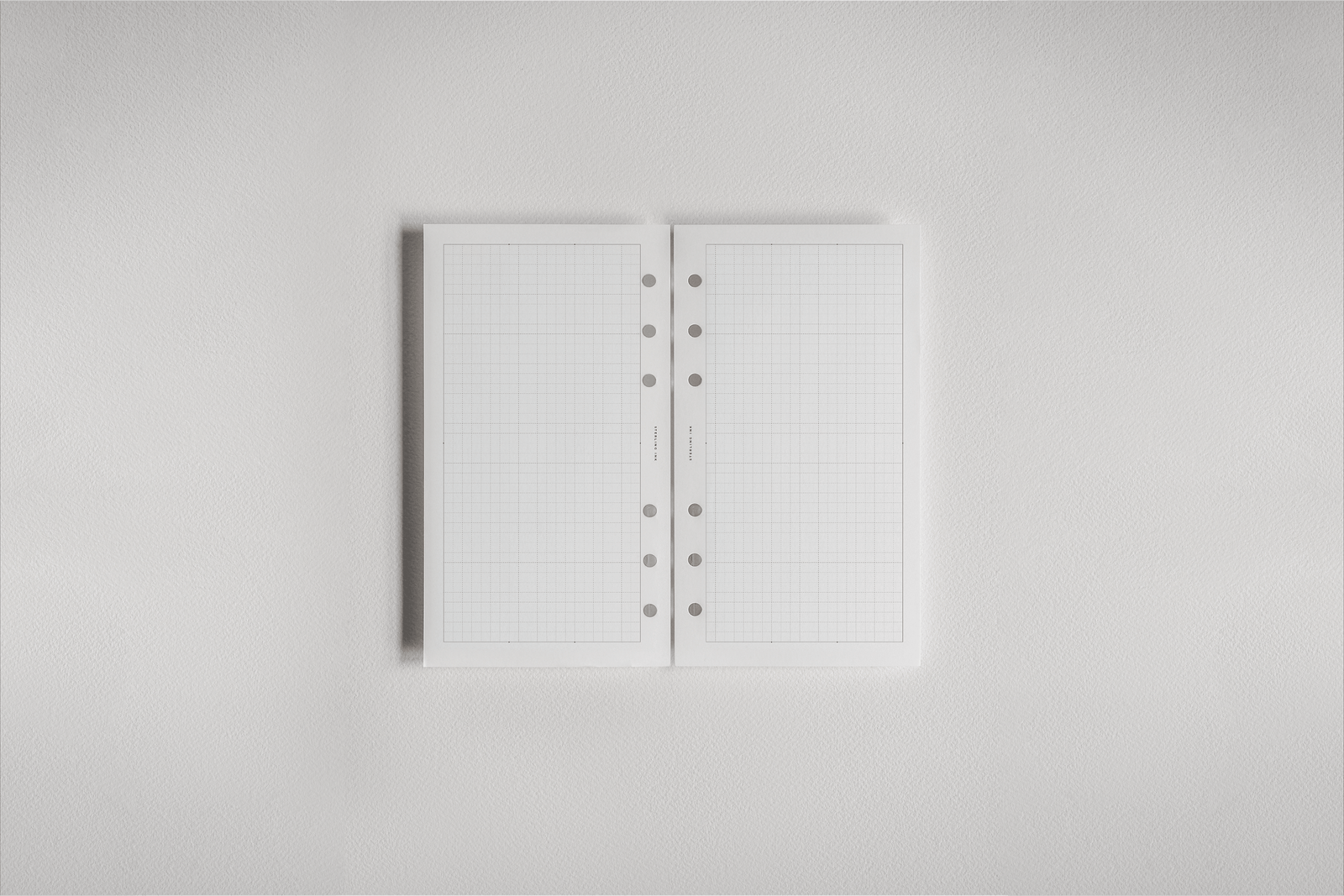 Open white gridded planner inserts, featuring light blue ruled lines and a spiral binding ring system for structured monthly scheduling.