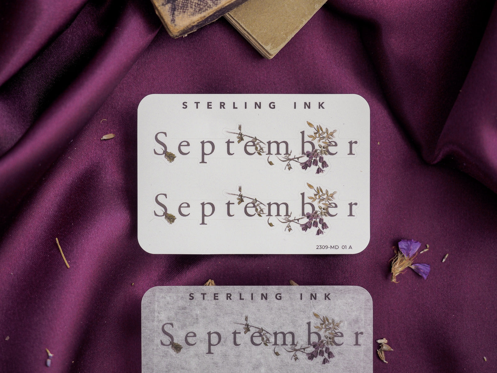 Decorative "September" month sticker featuring the word surrounded by delicate botanical drawings of dried wildflowers and herbs on a light, creamy background.