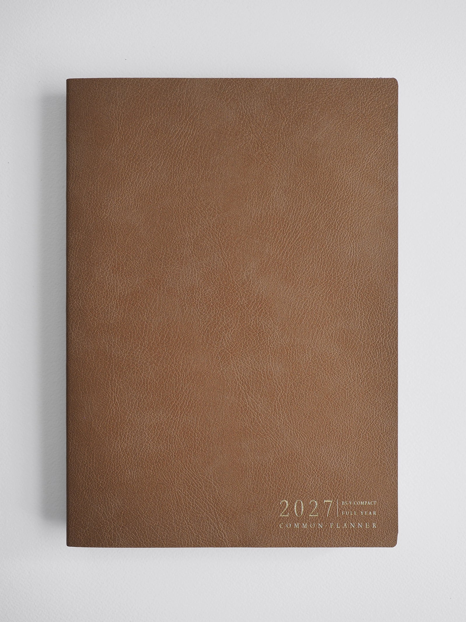 A brown textured faux-leather 2027 common planner with gold foil text in the bottom right corner, displayed on a light gray background.
#Color_Caramel