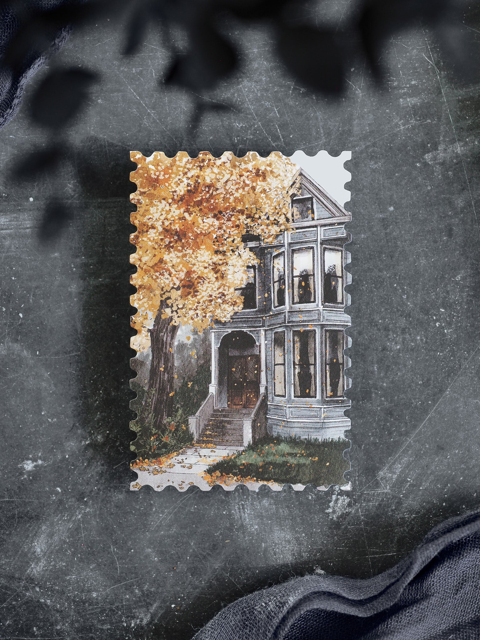 Autumnal die-cut sticker depicting a spooky, dilapidated mansion set against lush, golden fall foliage and yellow tree stamps.