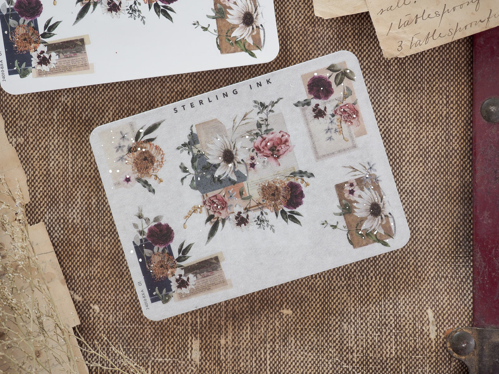 A sticker sheet adorned with muted vintage floral clusters, delicate greenery, and accented with shimmering silver foil corners.