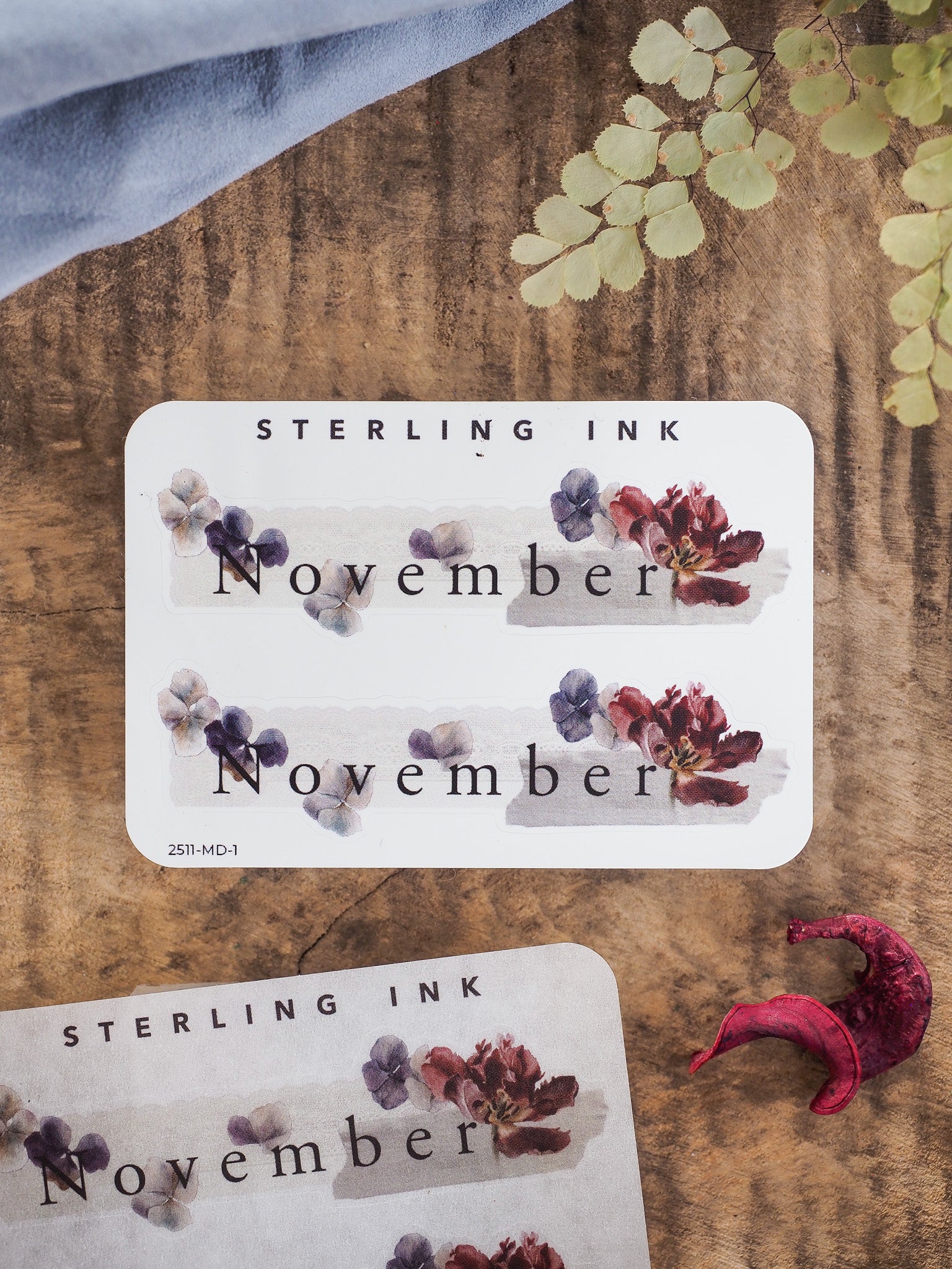 Autumnal sticker featuring the word "November" surrounded by realistic watercolor blooms in deep purple and rich burgundy tones.