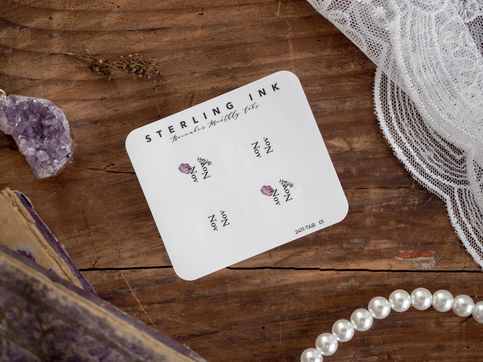 White planner tab card featuring "STERLING INK" branding and multiple sections labeled "NOV" with delicate purple floral illustrations for monthly organization in November 2024.