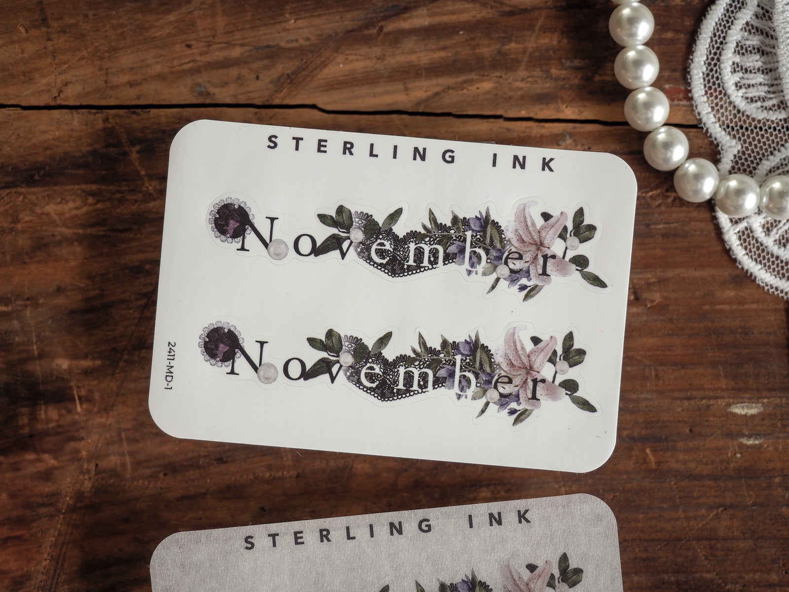 A coordinating month sticker for planning, featuring the word "November" centered within a delicate wreath of purple and dusty pink florals.