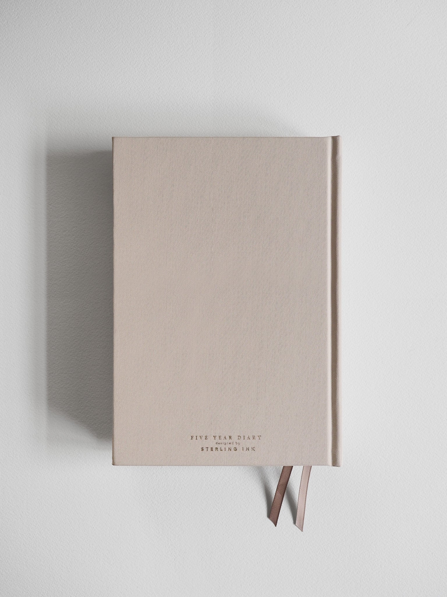 Minimalist A5 hardcover diary in soft, neutral beige, featuring subtle dark typography that indicates the five-year format.