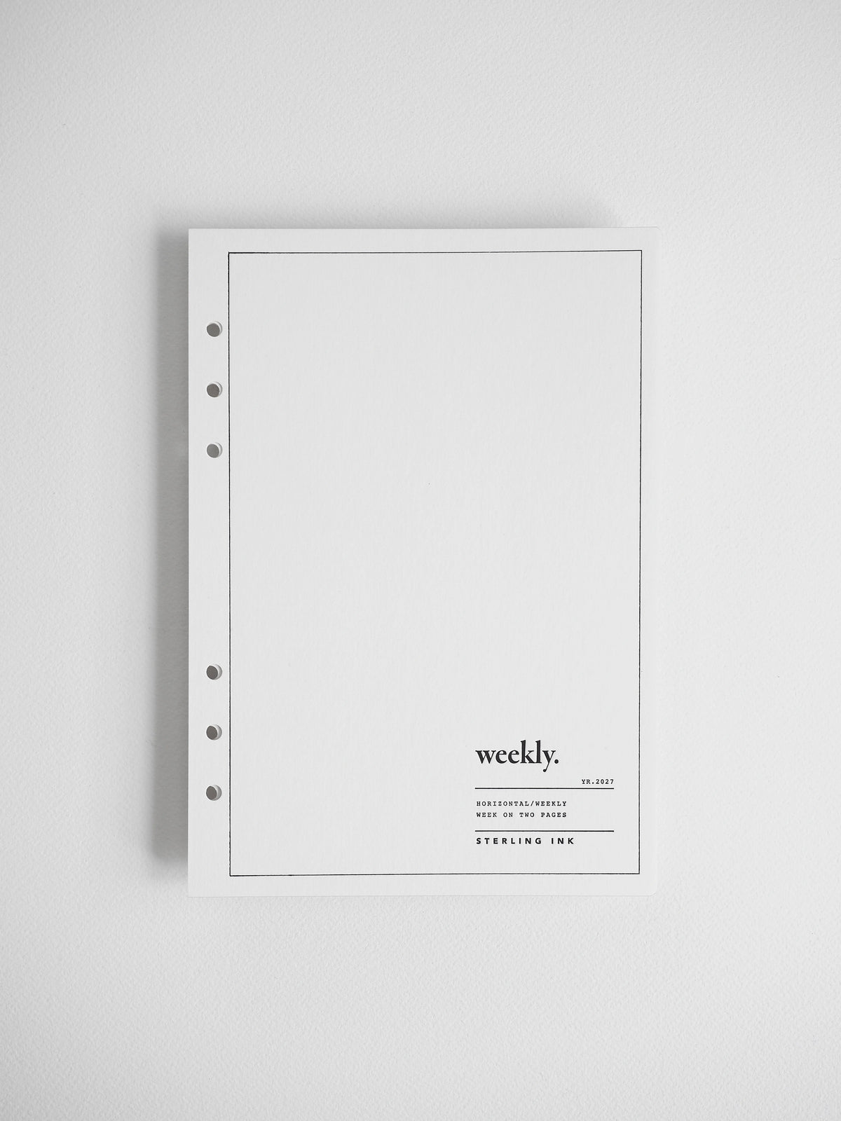 A minimalist white weekly planner or binder cover with a thin black border, five binder holes on the left, and small printed text reading 'weekly.' near the lower right, shown against a light gray background.
#Size_A5