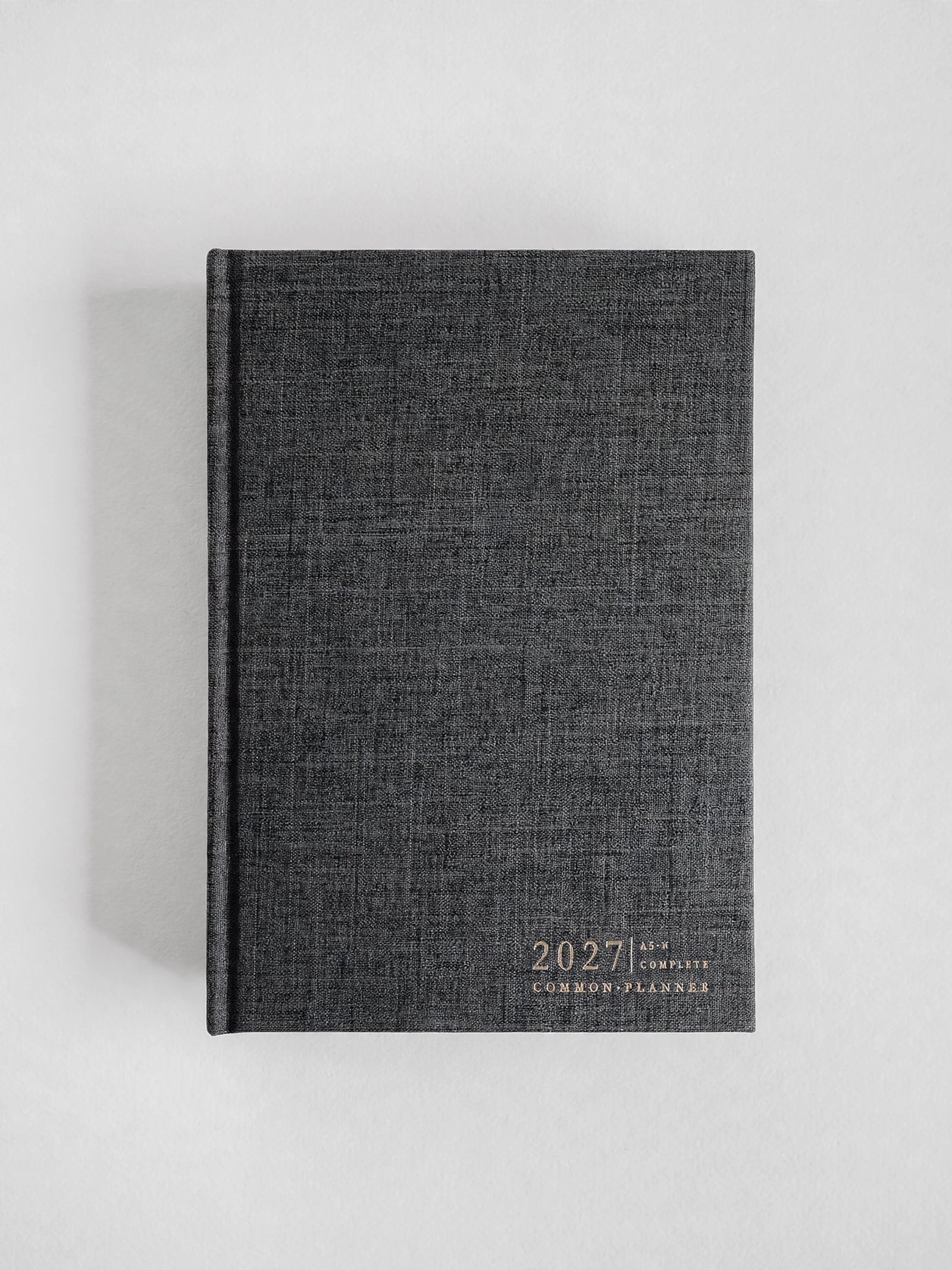 A dark gray linen-textured 2027 common planner with gold foil lettering, standing upright on a light gray background.
#Color_Charcoal