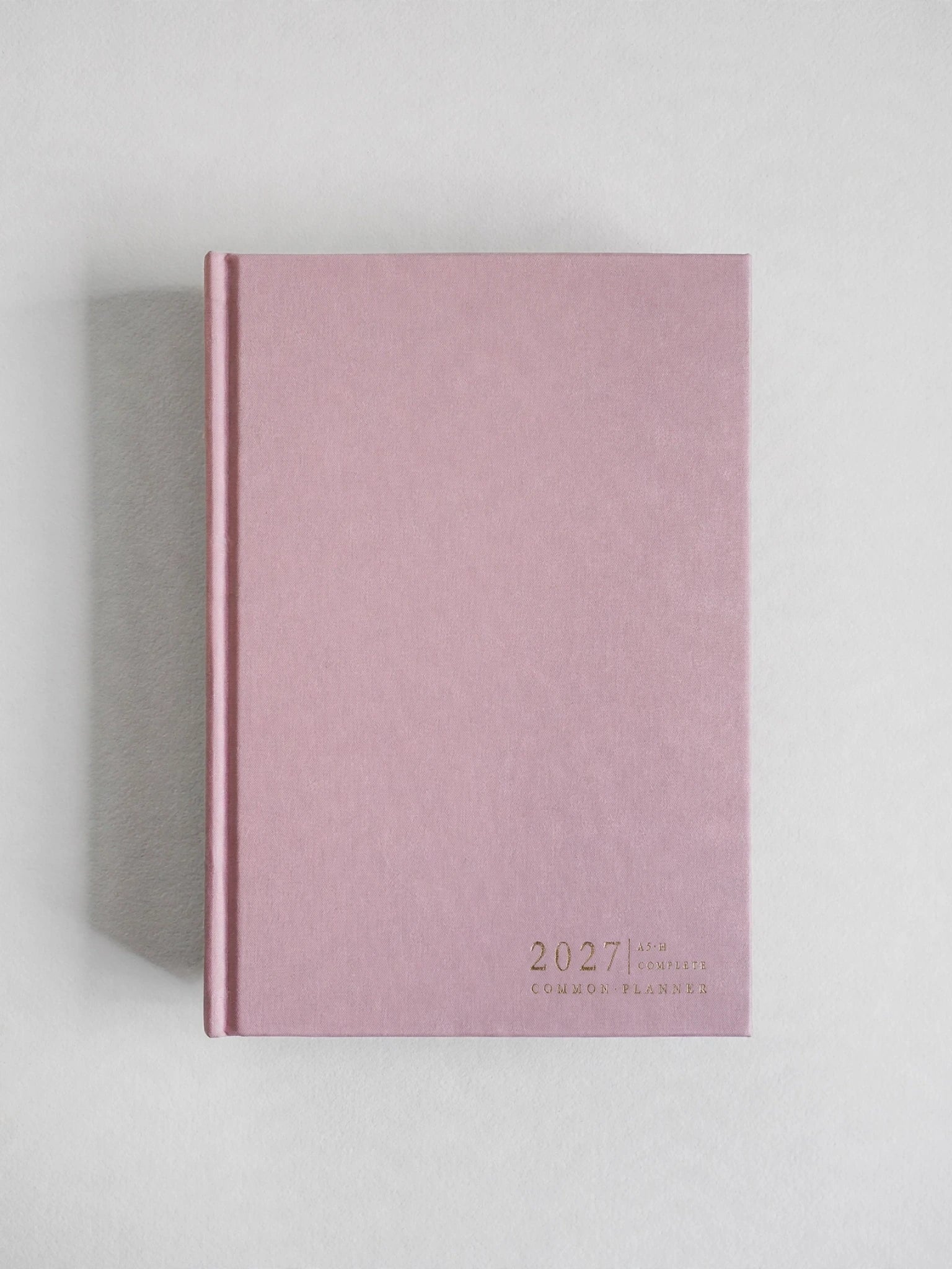 A dusty pink hardcover journal or planner for 2027, featuring gold foil text at the bottom right, photographed on a neutral light gray background with a soft shadow.
#Color_Seashell