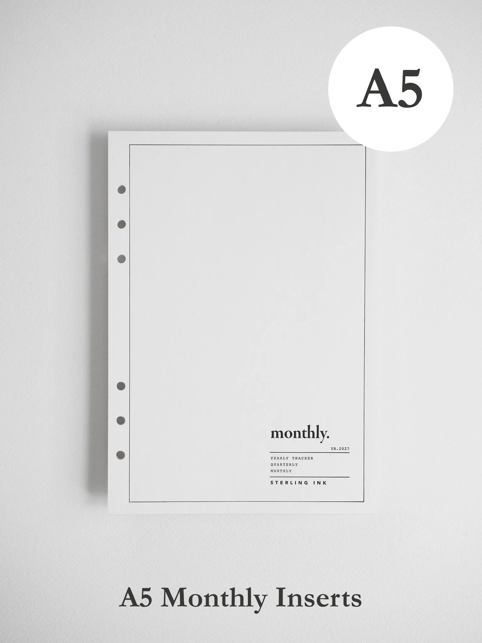 A white A5 monthly insert notebook page with a thin border, five binder holes on the left, and the word 'monthly.' printed near the bottom, shown on a light gray background.
#Size_A5