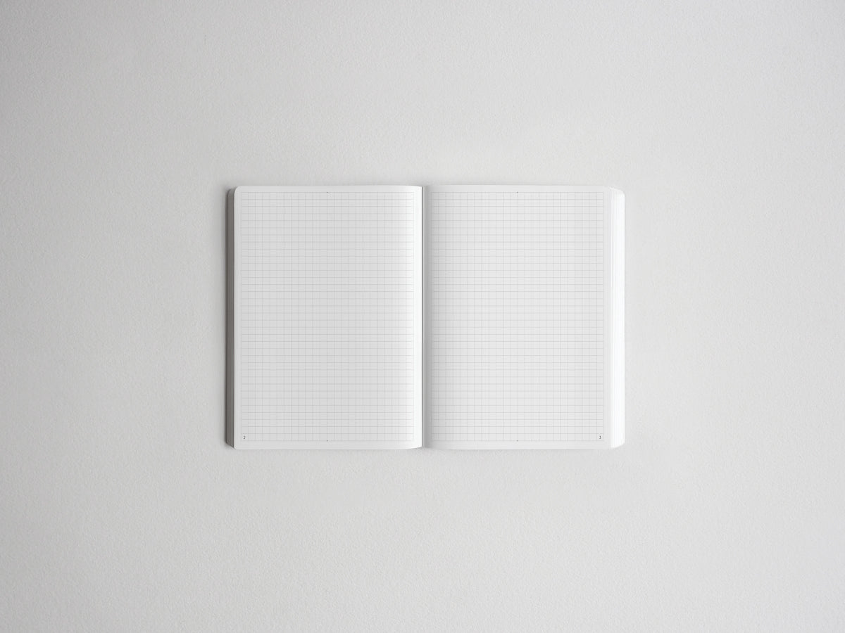 An open white grid notebook with blank pages, photographed from above on a light gray background.