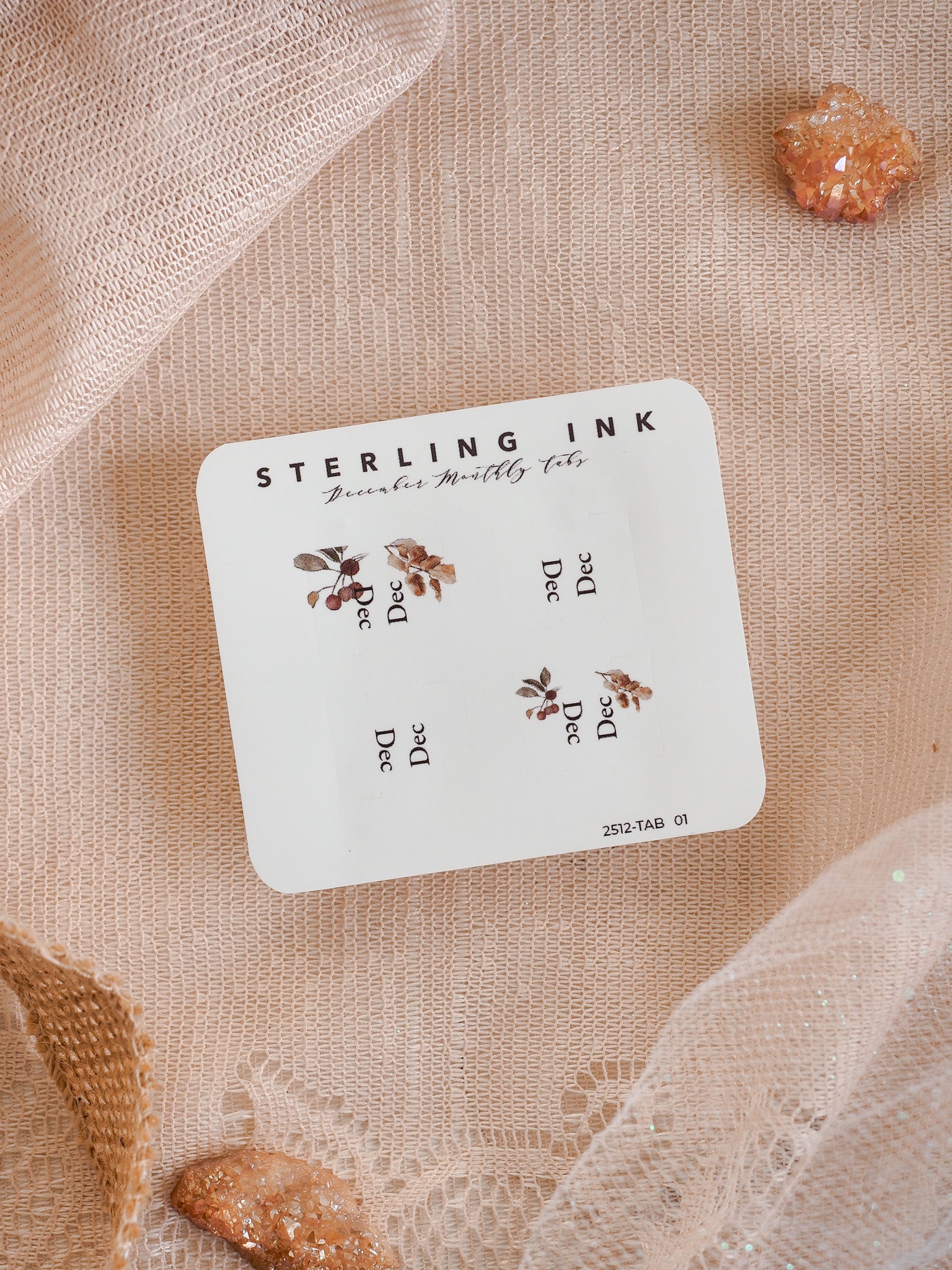 White decorative planning tabs for December 2025, featuring the Sterling Ink brand name and elegant printed clusters of autumnal leaves.