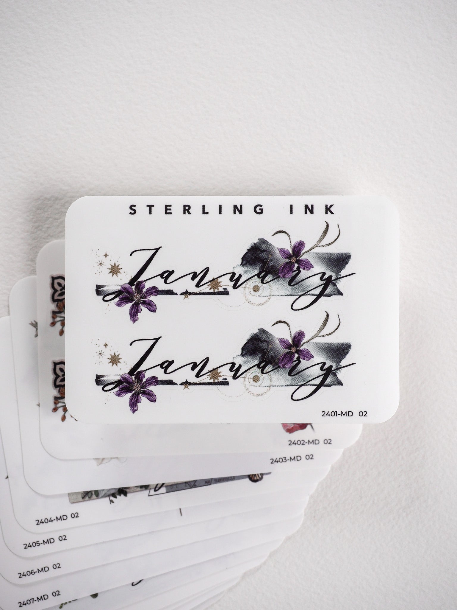 Watercolor floral month stickers for planners, featuring elegant script lettering and delicate purple and gray blossoms.