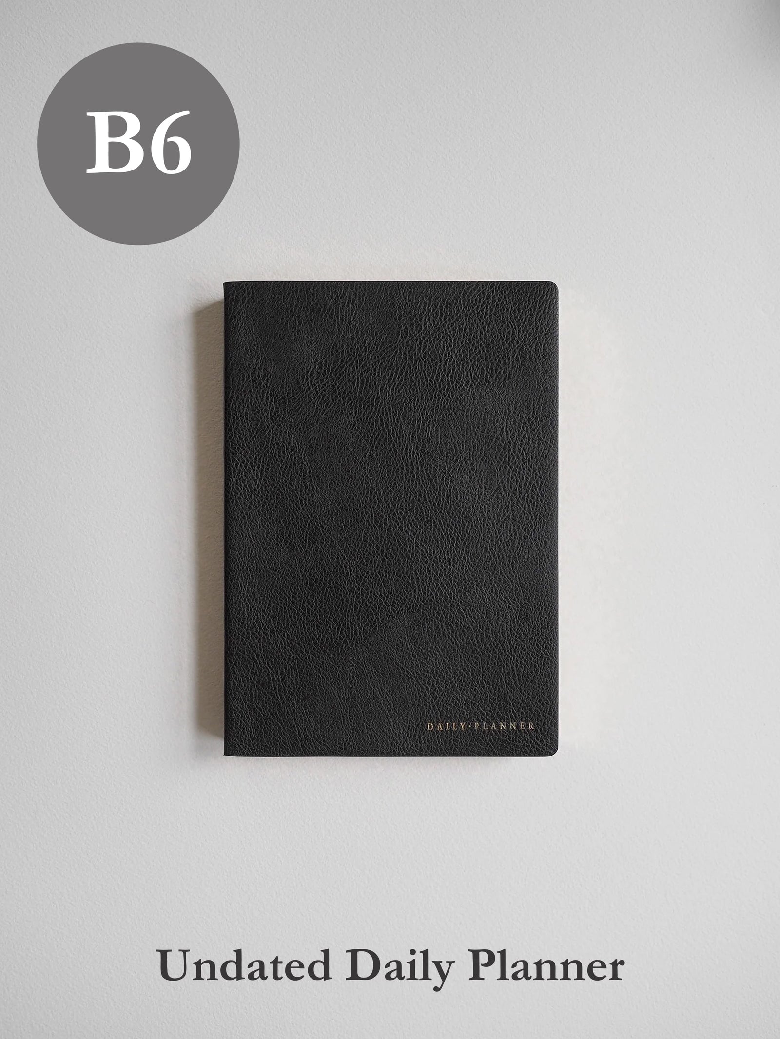 Sleek B6 undated daily planner featuring a textured, dark charcoal matte cover with minimal, elegant branding detail.