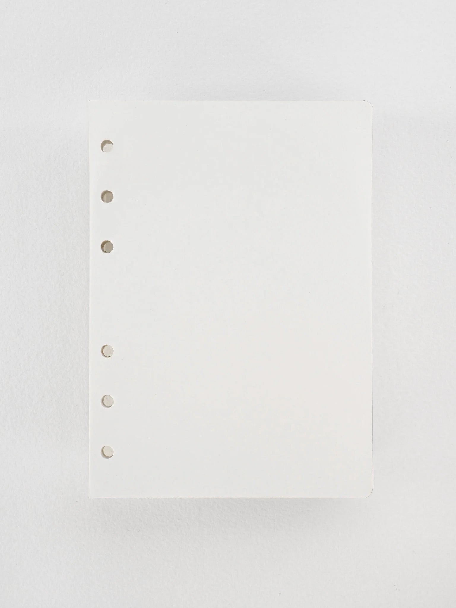 Plain white loose leaf inserts of high-quality Tomoe River paper, featuring several finger-punched holes designed for ring binding.
