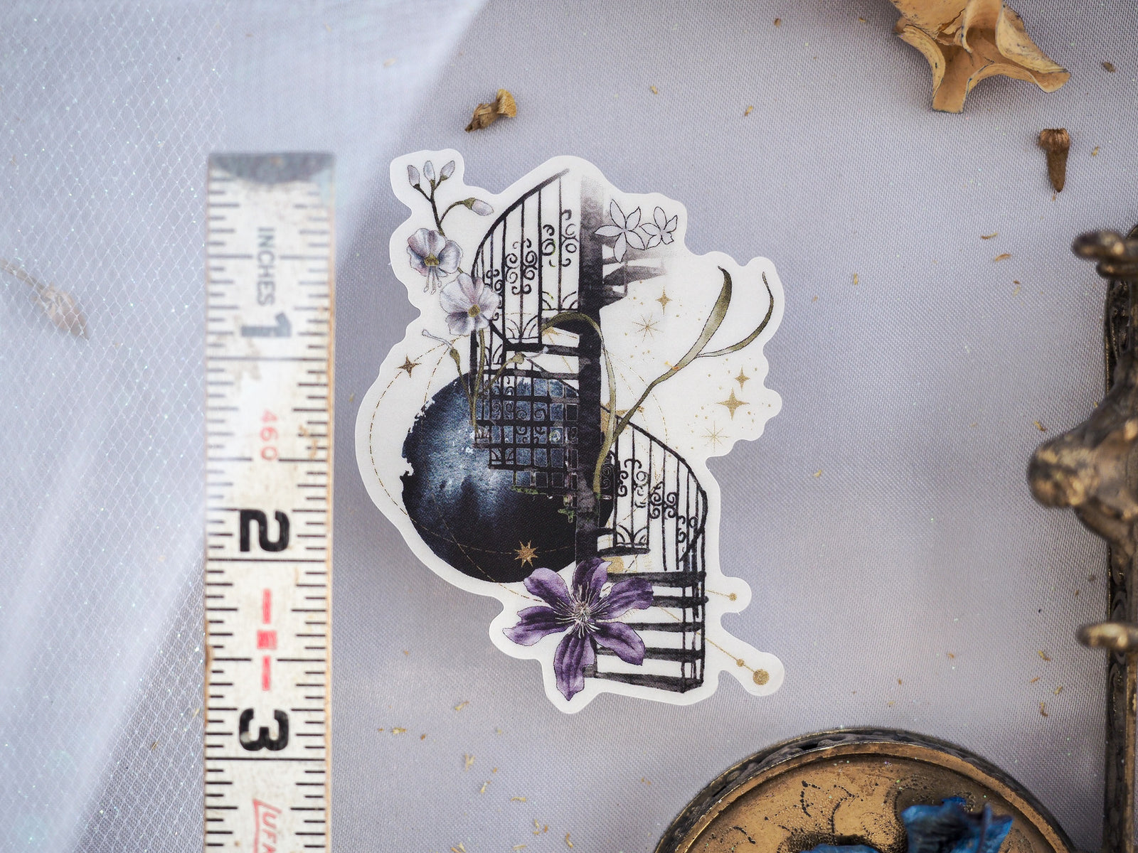Ornate die-cut sticker featuring a black wrought-iron gate entwined with delicate branches and vivid purple and white spring flowers for creative journaling.