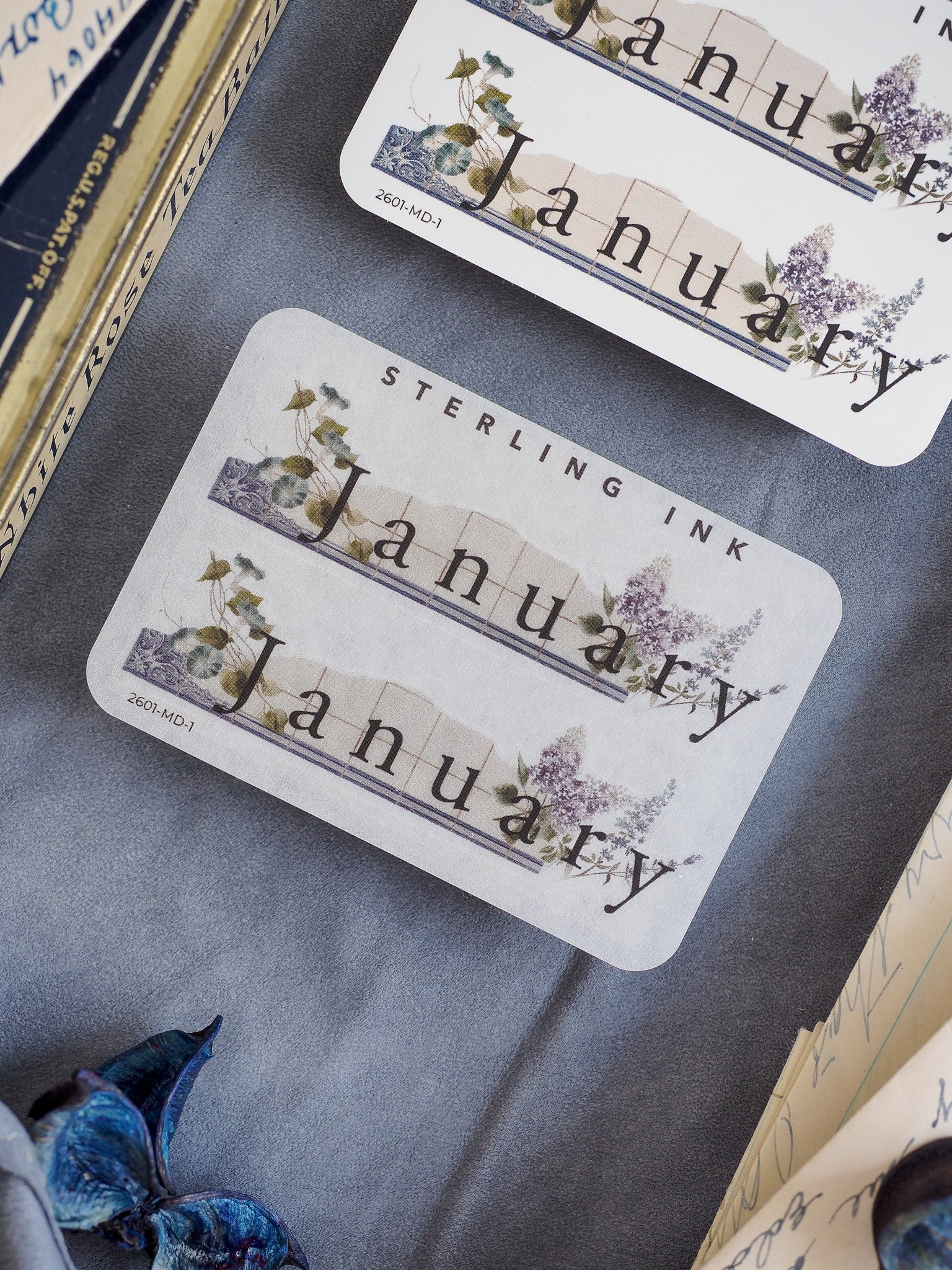 Elegant "January" month sticker with "Sterling Ink" text, featuring delicate watercolor floral accents of purple and green foliage.