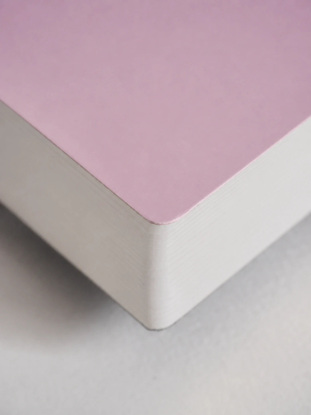 A close-up of a notebook or book corner showing a dusty pink top cover and white stacked pages, photographed on a light neutral surface.
#Color_Fairyfloss